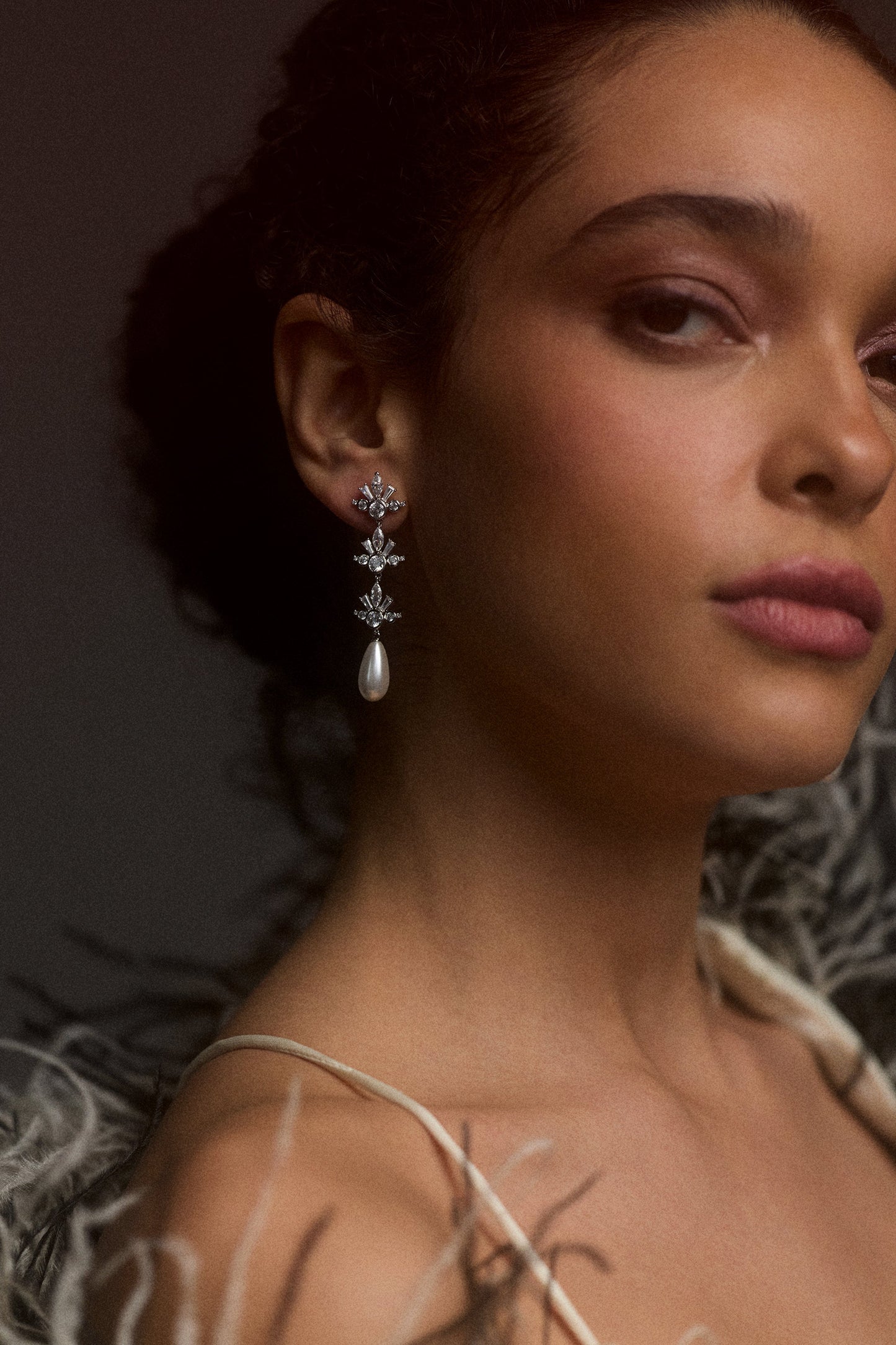 A MODEL LOOKING AT THE CAMERA TURNED SLIGHTLY TO THE SIDE, WITH HER HAIR IN A BUN AND WEARING THE UNDER THE SEA PEARL TRIPLE DROP EARRINGS STYLED WITH A FUR JACKET
