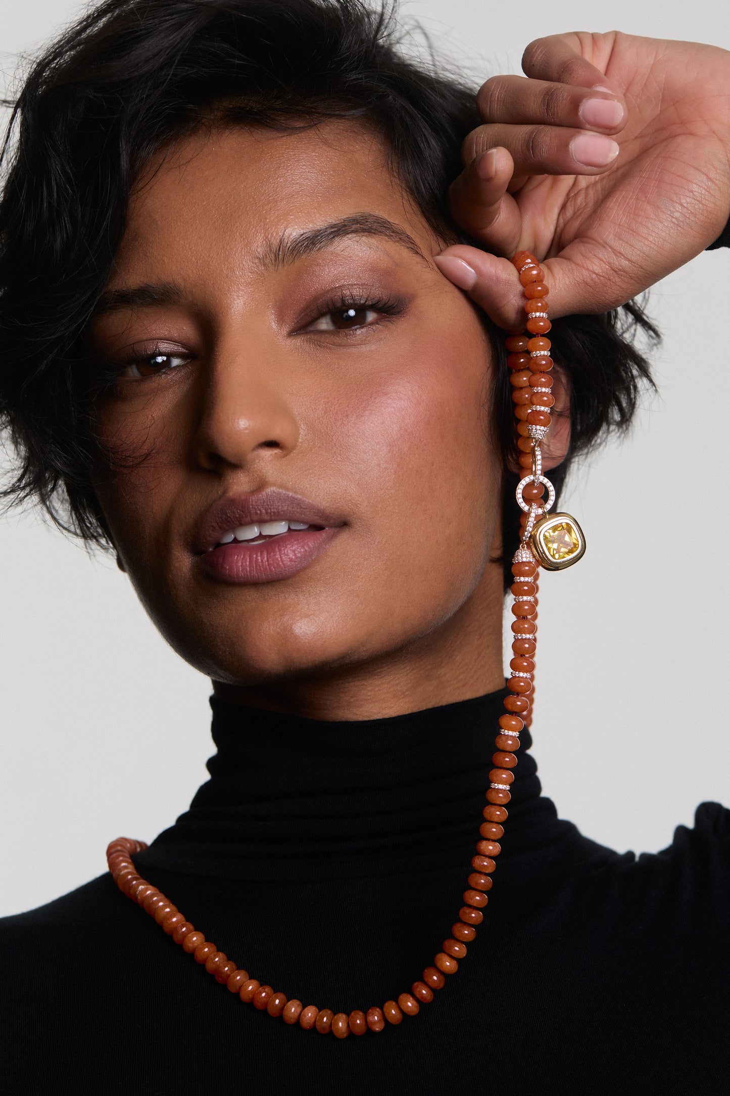 A MODEL IN A BLACK TURTLENECK HOLDING THE BOUJEE BEADS CARNELIAN LARGE NECKLACE UP TO HER FACE
