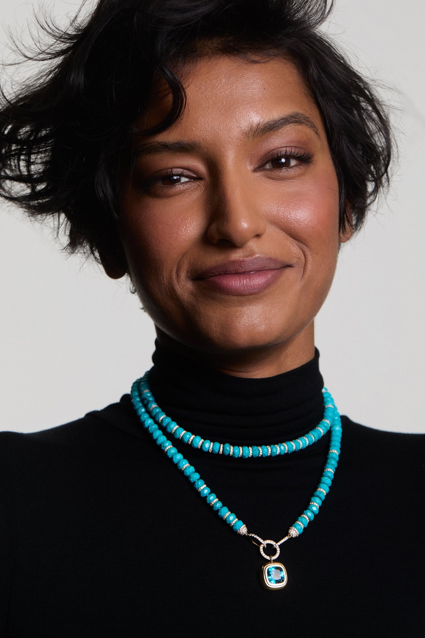 A MODEL IN A BLACK TURTLENECK SMILING AT THE CAMERA WEARING THE BOUJEE BEADS TURQUOISE LONG NECKLACE