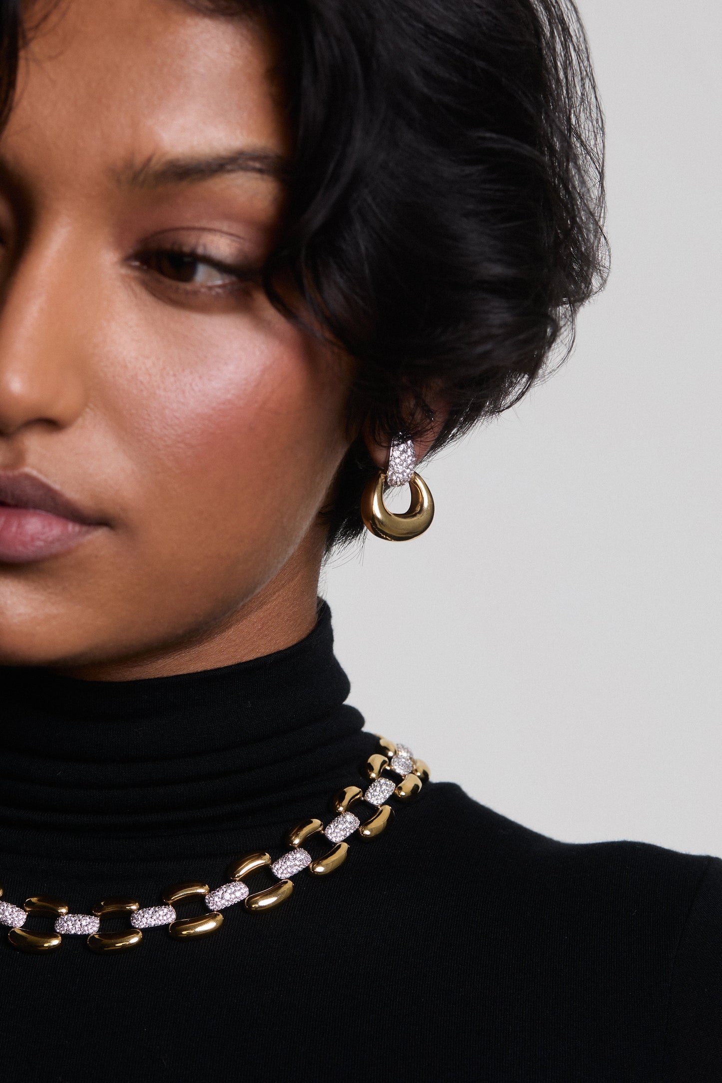 HALF OF A MODEL’S FACE IN FRAME, AS SHE WEARS THE EDIE DOOR KNOCKER EARRINGS AND EDIE COLLAR NECKLACE