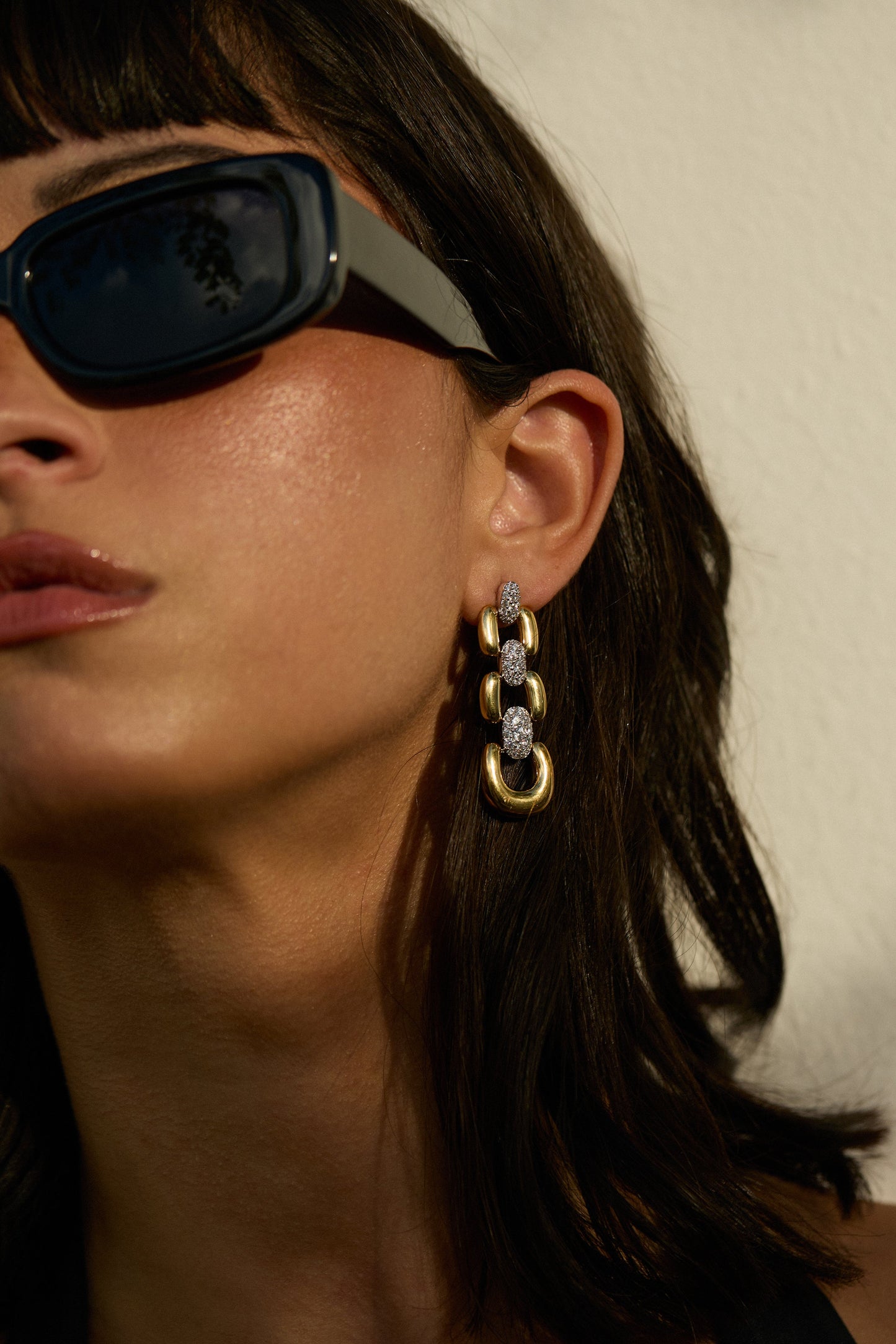 HALF OF A MODEL’S FACE IN FRAME, AS SHE WEARS BLACK SUNGLASSES AND THE EDIE LINEAR EARRINGS
