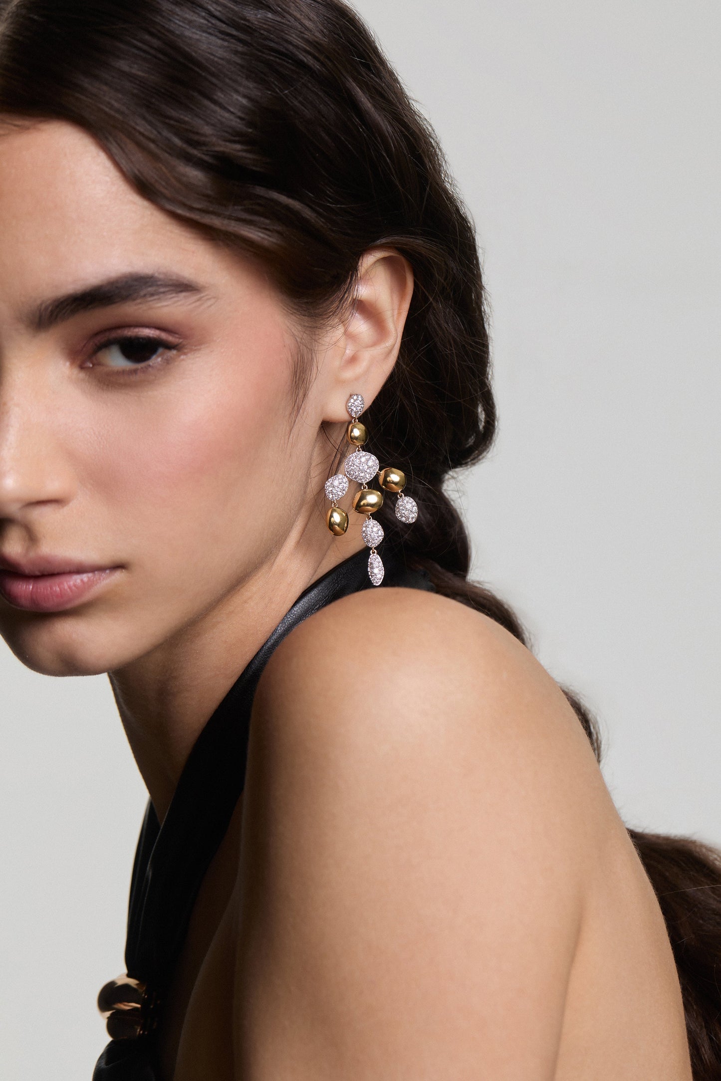 A MODEL LOOKING AT THE CAMERA WITH HALF OF HER FACE IN FRAME, WEARING THE PEBBLES CHANDELIER EARRINGS AND HER HAIR TUCKED BEHIND HER EAR