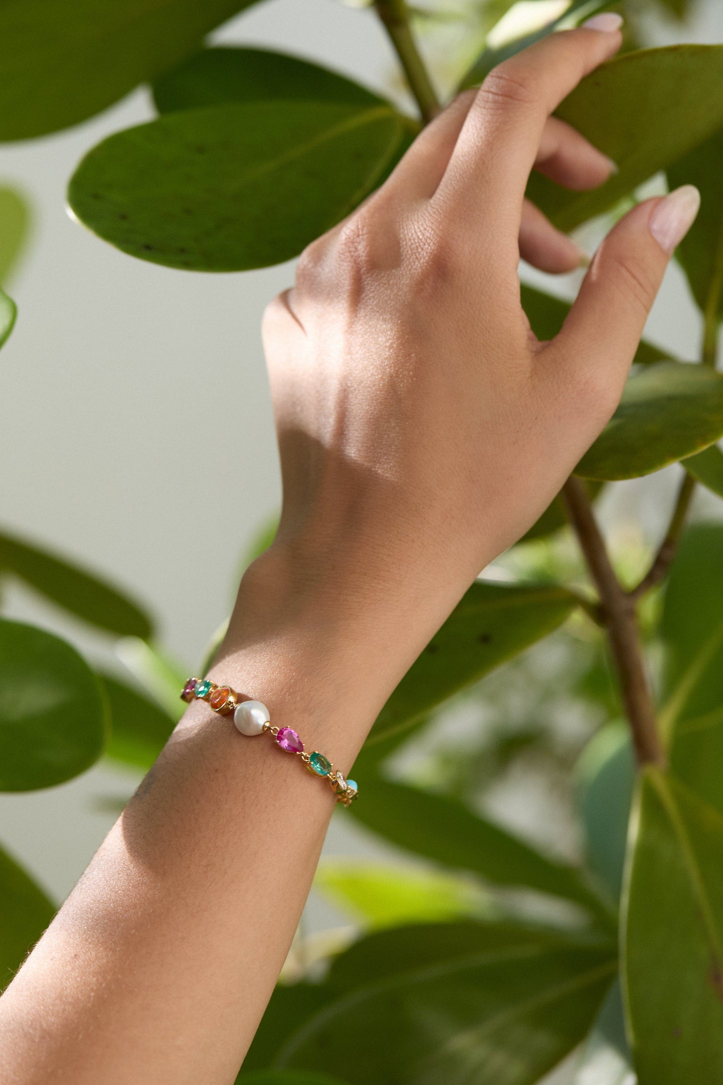 A LIFTED HAND TOUCHING A LEAFY PLANT, WEARING THE FRIEDA FRESHWATER PEARL CHAIN BRACELET