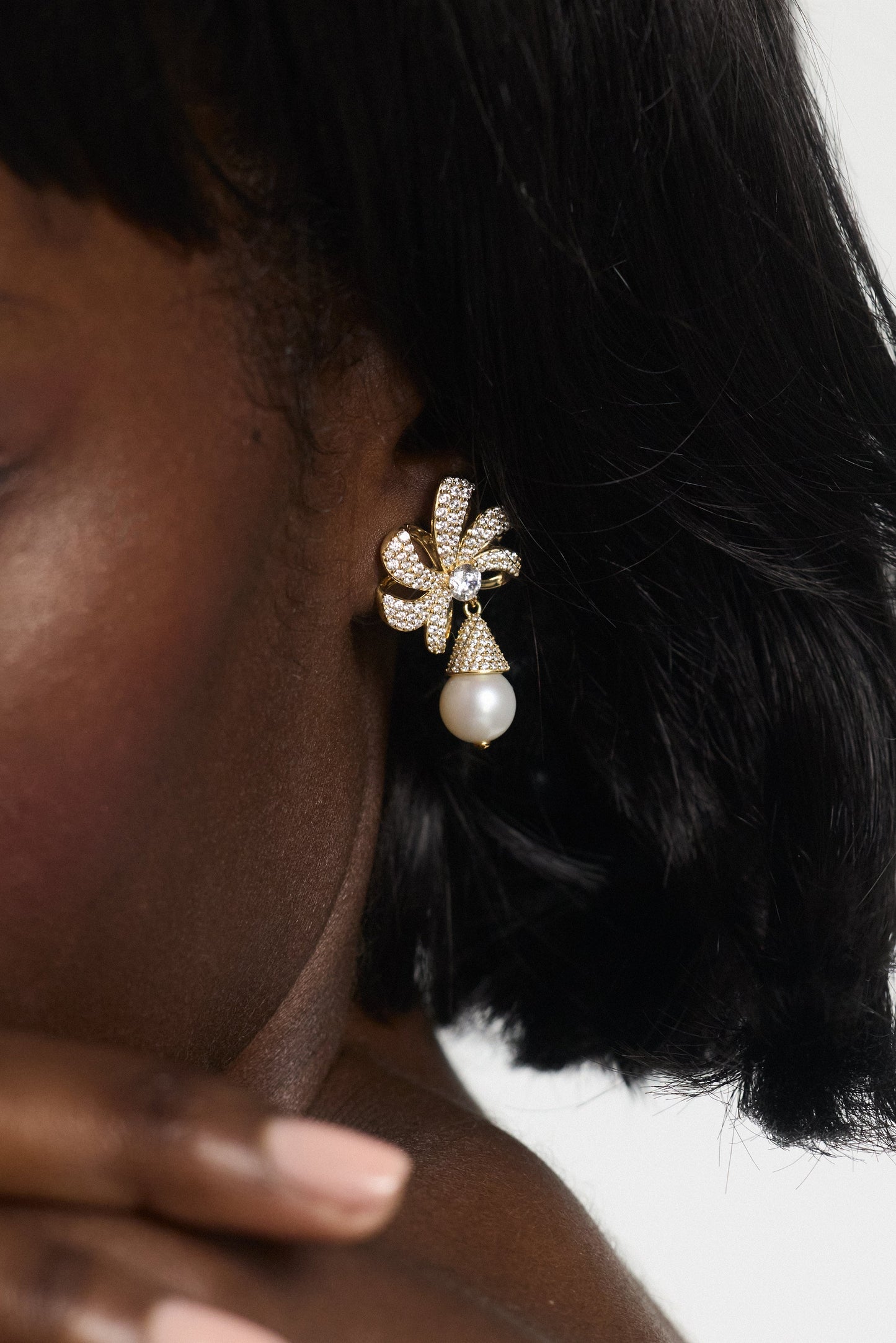 CLOSE UP OF A MODEL’S EAR WEARING THE EROS PEARL DROP POST EARRINGS, WITH HER BLACK HAIR COVERING THE TOP OF HER EAR