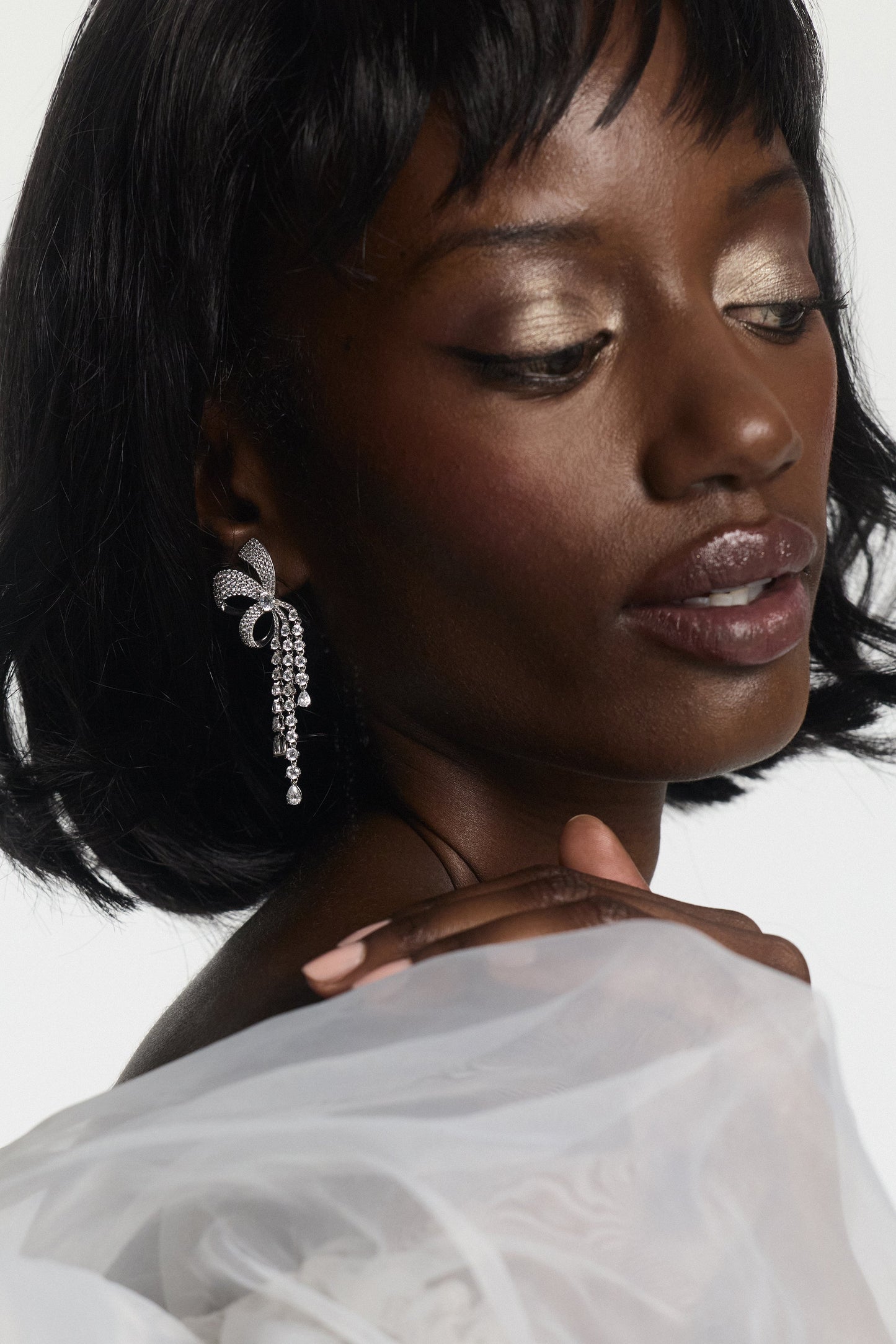 CLOSE UP OF A MODEL LOOKING DOWN WEARING THE EROS RIBBON CHANDELIER EARRINGS, WITH HER HAND ON HER SHOULDER