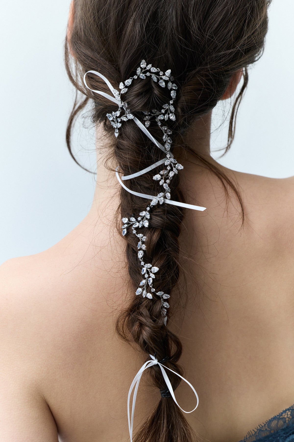 CLOSE-UP OF A WOMAN’S BACK WITH A LONG BRUNETTE BRAID, FEATURING NADRI’S VINES HAIR GARLAND WOVEN THROUGH THE TWISTS AND TURNS OF THE BRAID.