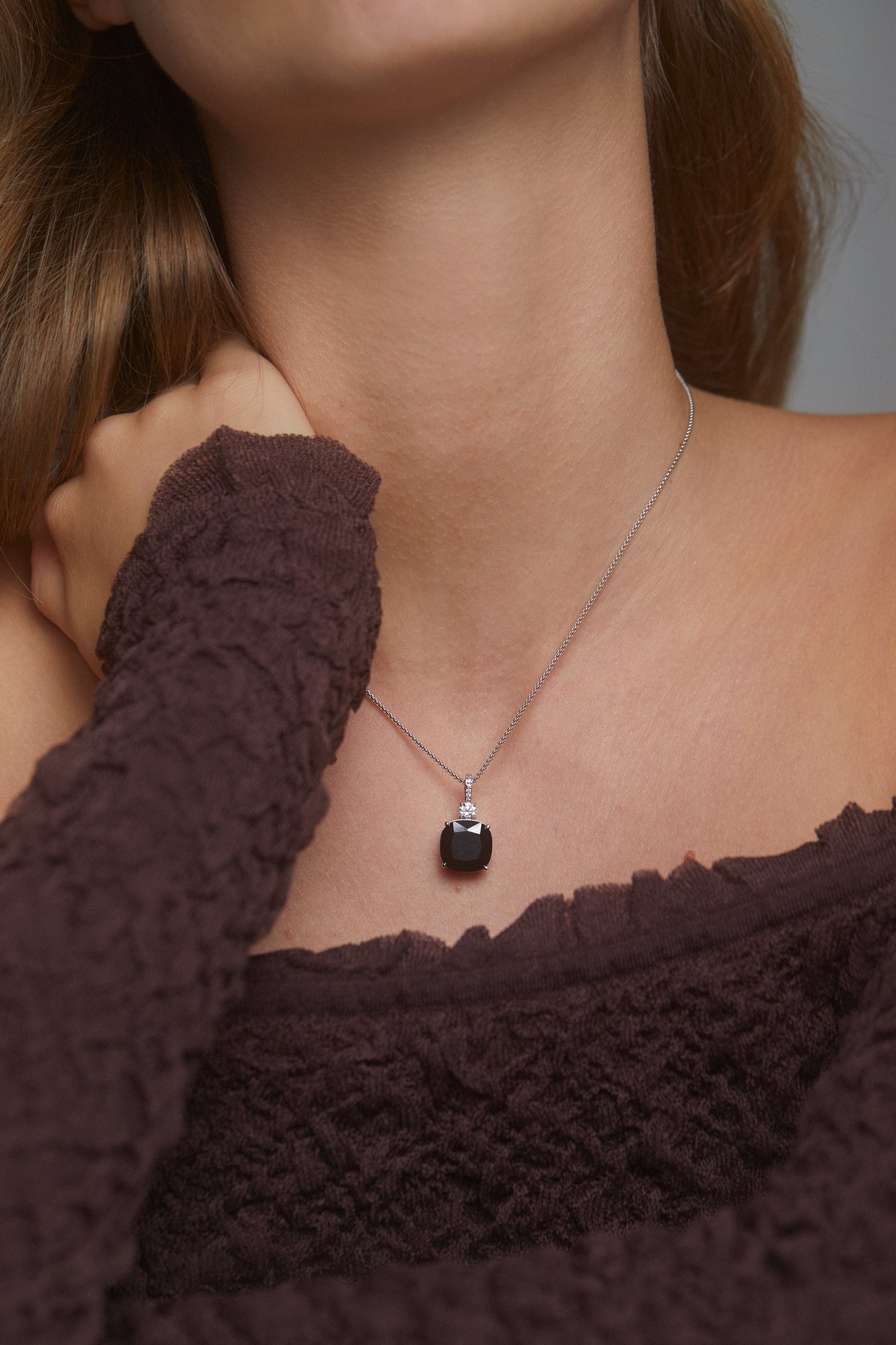 CLOSEUP IMAGE OF MODEL WEARING OUR MACARON BLACK CUSHION CZ PENDANT WITH A BROWN OFF THE SHOULDE TOP.  HER HAND IS ON HER SHOULDER IN A RELAXED POSE.