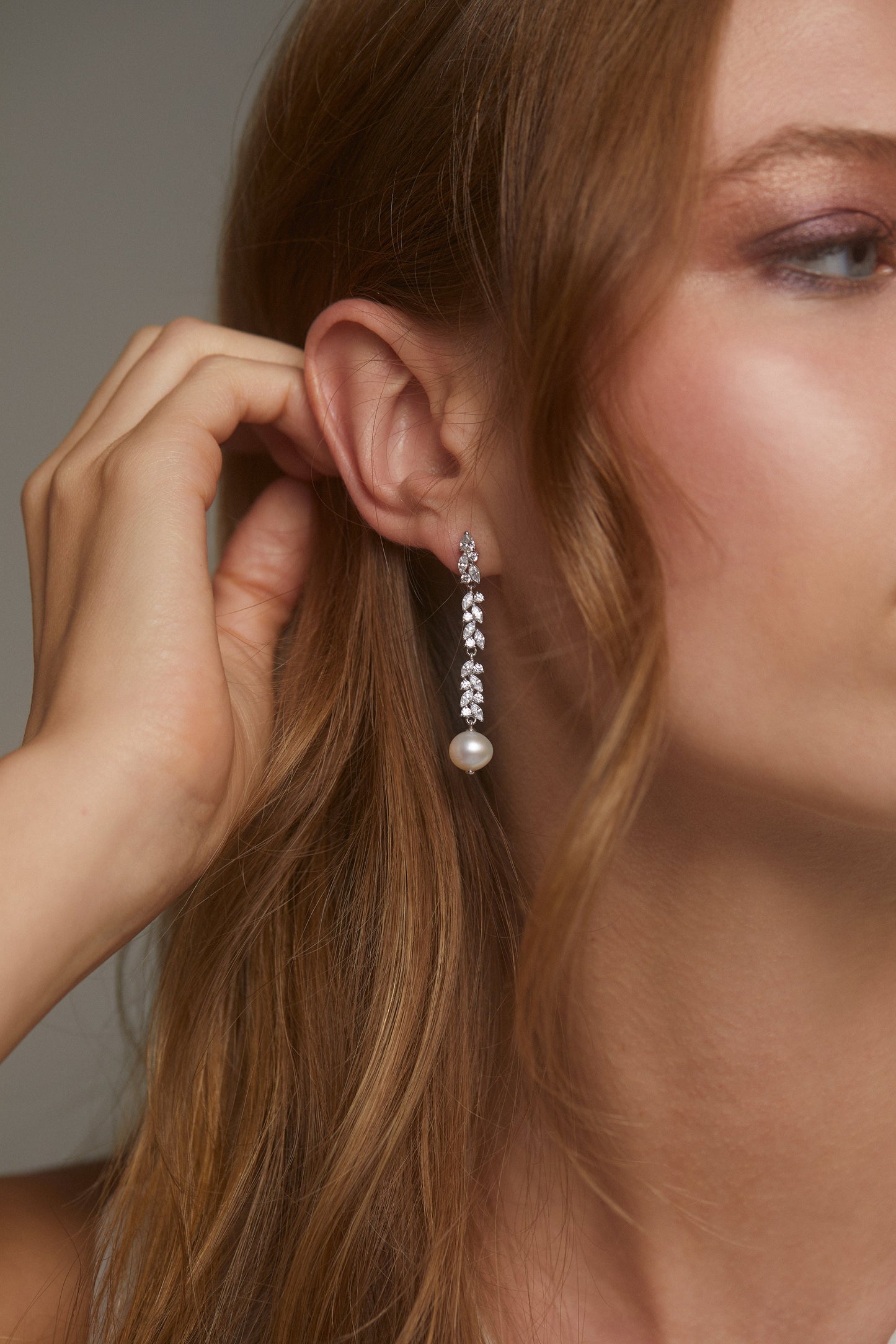SAVANNAH LINEAR WITH PEARL EARRINGS ON MODEL.ONLY HALF OF HER FACE IS SHOWING WHILE SHE PULLS HER HAIR BACK BEHIND HER EARS. 