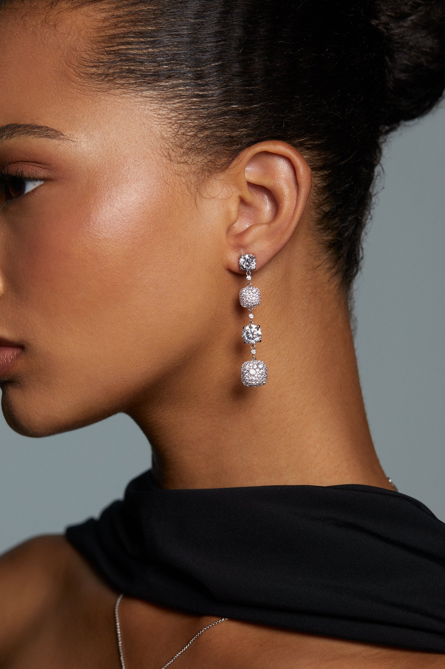 SIDE VIEW OF MODEL WEARING CRUSHED CUSHION LINEAR EARRINGS. HER HAIR IS PULLED BACK INTO A BUN AND SHE IS WEARING A SILK BLACK SCARF.