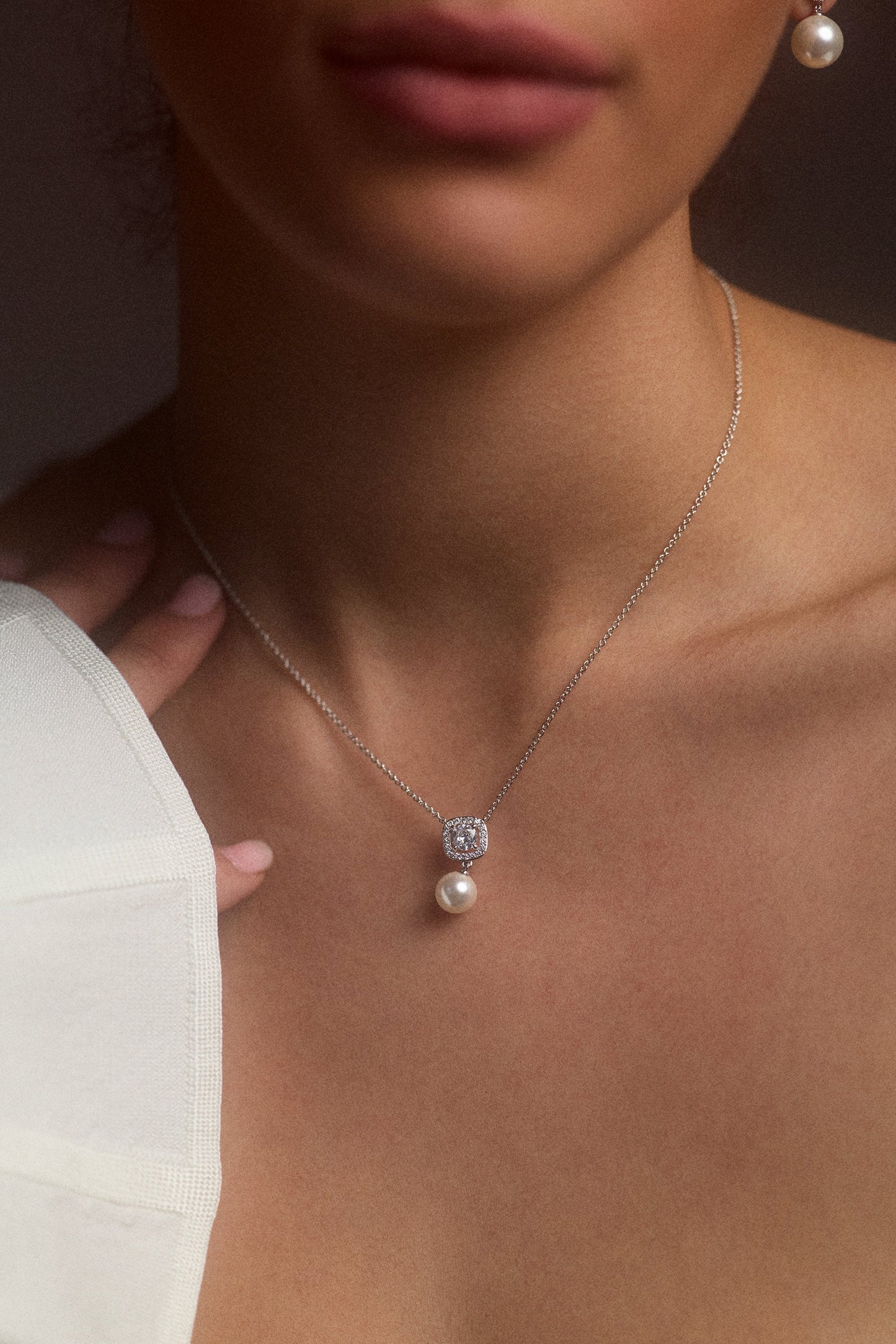 CLOSE UP OF A MODEL’S CHEST WITH HER HAND UP TO HER NECK, WEARING THE UNDER THE SEA CUSHION HALO PEARL NECKLACE