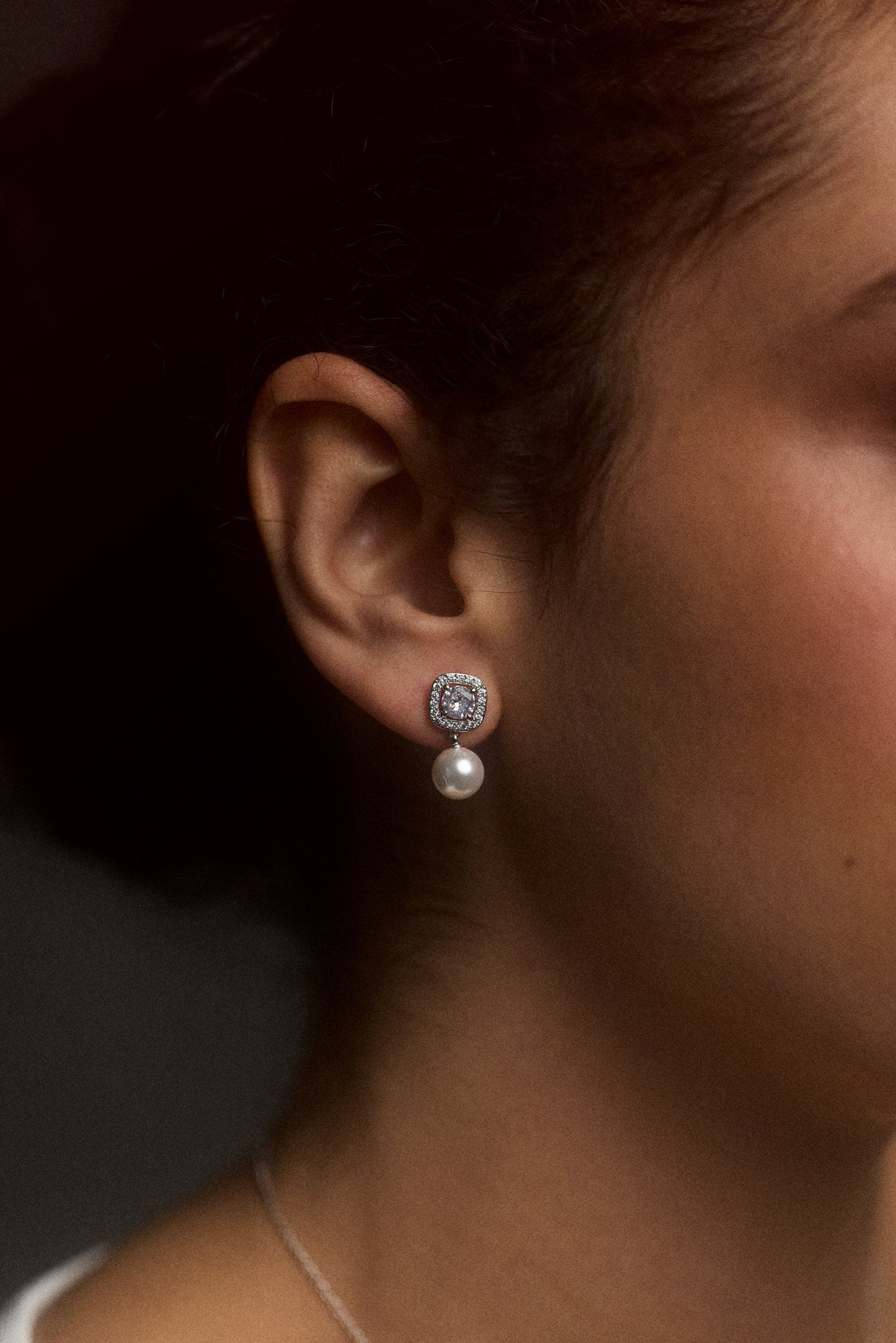 CLOSE UP OF A MODEL’S EAR WEARING THE UNDER THE SEA CUSHION HALO PEARL DROP EARRINGS