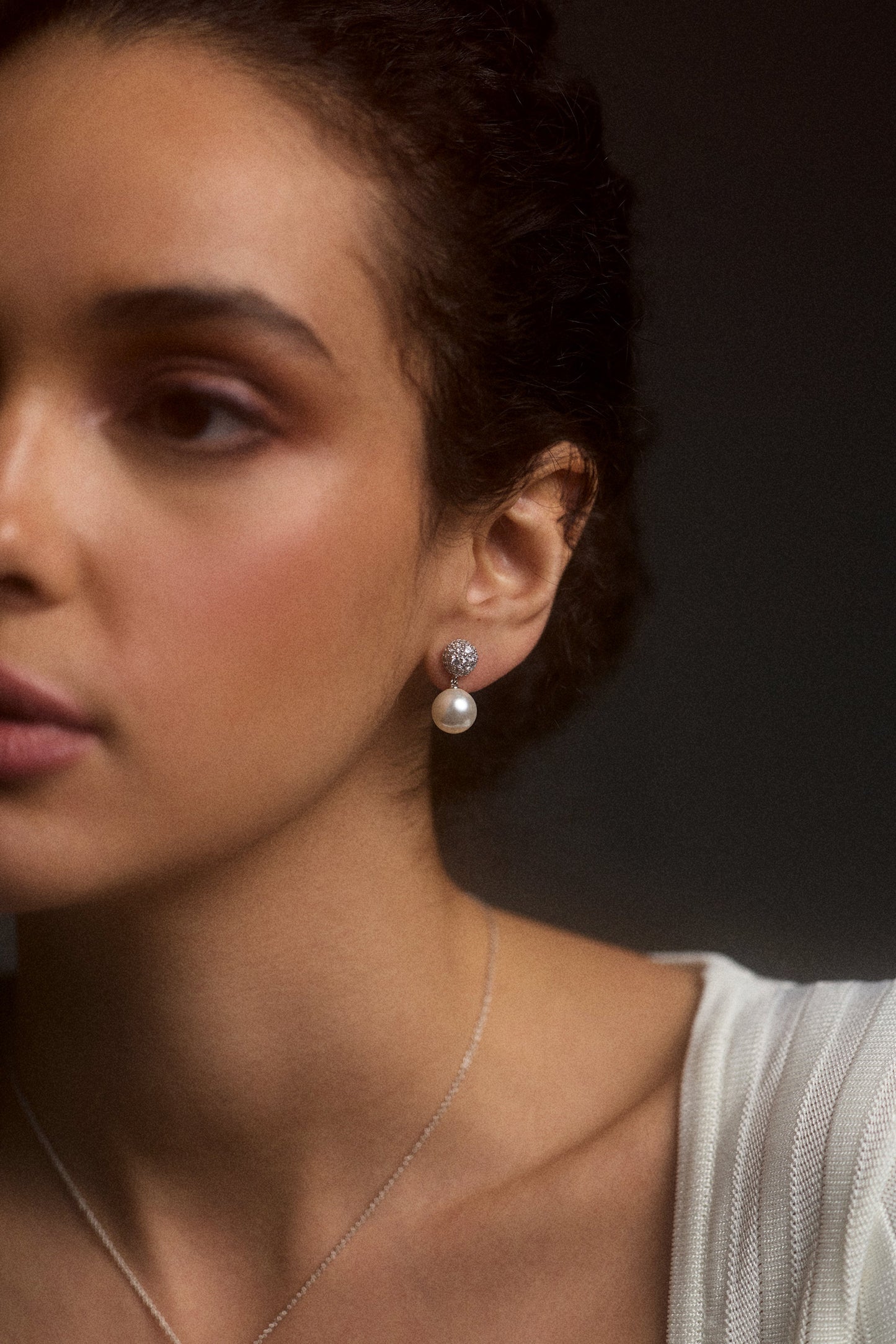 CLOSE UP OF HALF OF A MODEL’S FACE WEARING A WHITE TOP AND THE UNDER THE SEA PAVE PEARL DOUBLE DROP EARRINGS