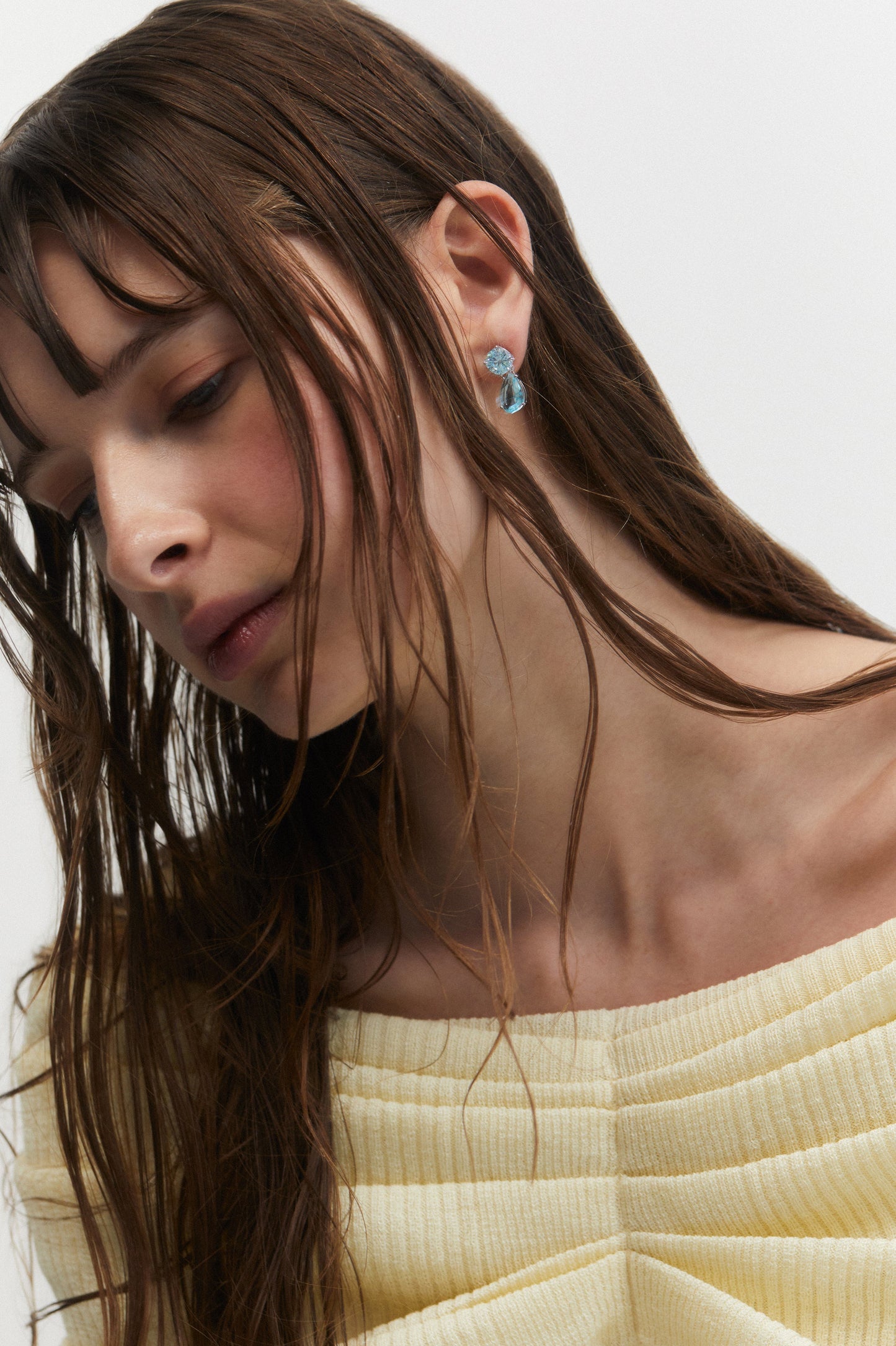 A MODEL LOOKIN DOWN TO THE SIDE WEARING MAIDEN AQUA PEAR DROP EARRINGS AND A YELLOW TOP