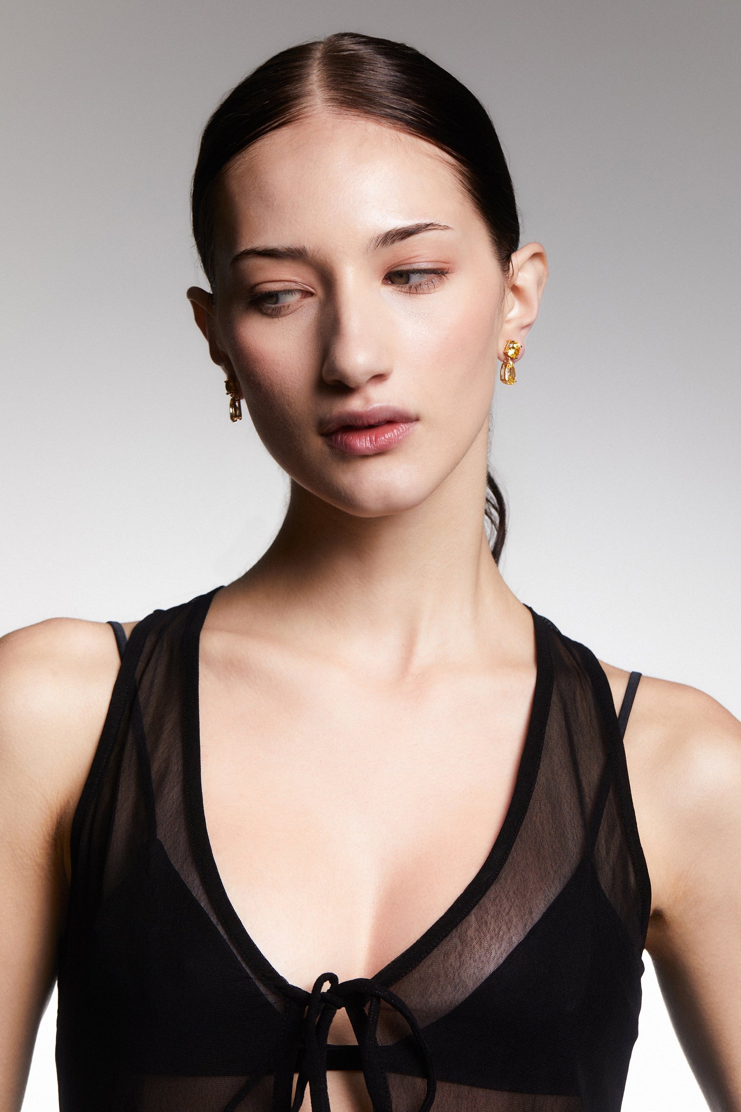 WIDE SHOT OF A MODEL WEARING MAIDEN YW PEAR DROP EARRINGS, HER HAIR IN A PONYTAIL, AND WEARING A BLACK MESH TOP