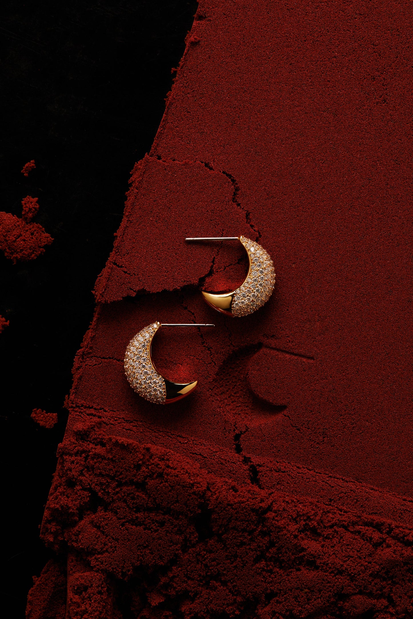 EDITORIAL STILL OF ALMA DOME J HOOP EARRINGS ON RED SAND. 
