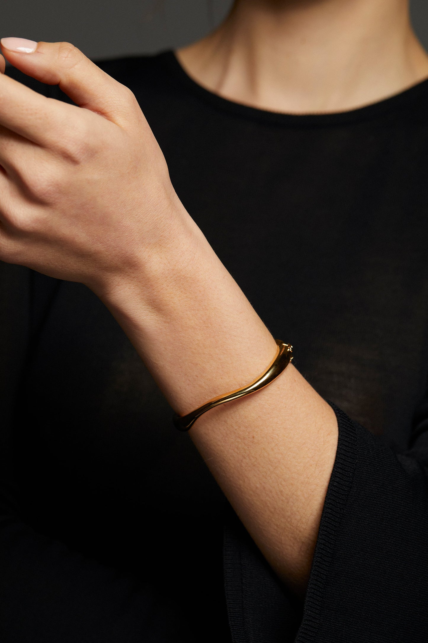 MODEL WEARING ALMA METAL ORGANIC HINGE BRACELET. SHE HAS ON A BLACK LONG SLEEVE TOP - IT IS A CLOSE UP IMAGE OF HER ARM WITH THE HINGE BRACELET ON HER WRIST.