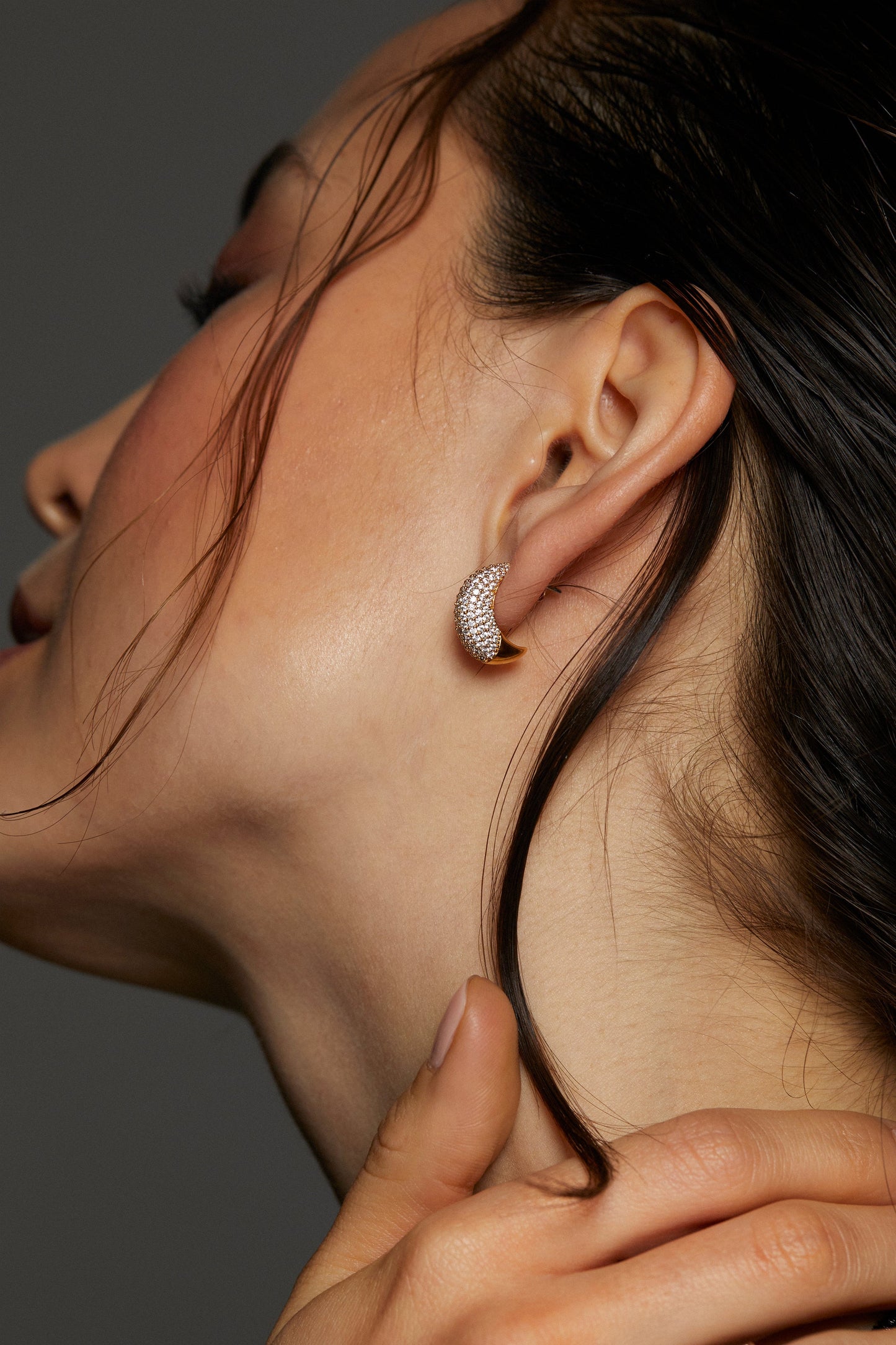 CLOSE UP IMAGE OF MODEL WEARING ALMA DOME J HOOP EARRINGS. SHE IS FACING AWAY FROM THE CAMERA WITH EYES CLOSED AND HAIR TUCKED BEHIND HER EAR.