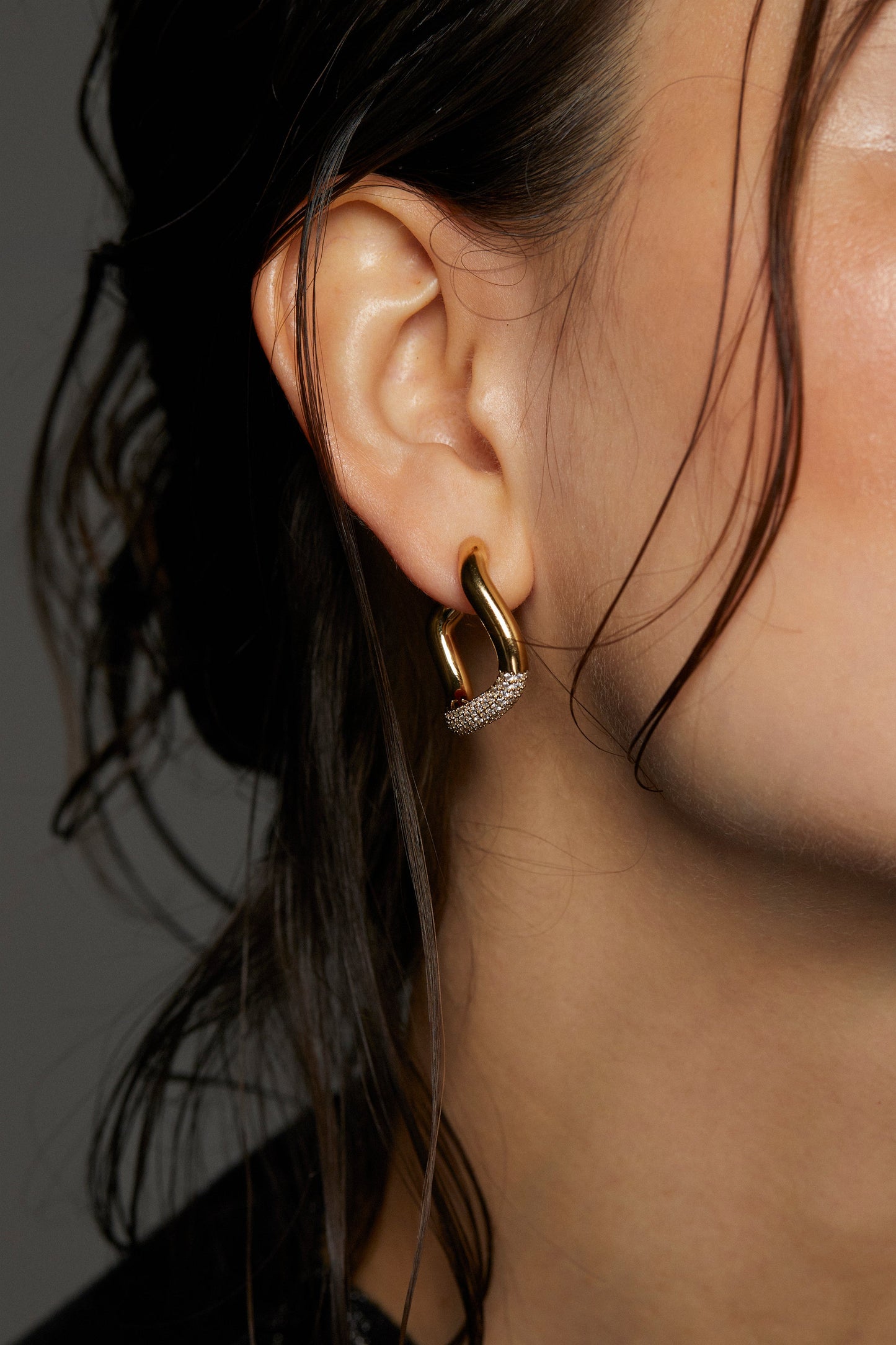 CLOSE UP IMAGE OF ALMA PAVE ORGANIC C HOOP EARRINGS ON MODEL. IT IS A TIGHT SHOT OF HER EAR WITH HER HAIR PULLED BACK IN A LOSE BUN. 