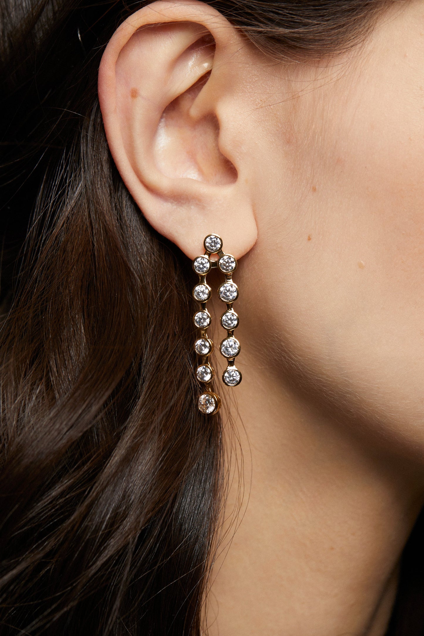 MODEL WEARING BROOKLYN DOUBLE LINEAR EARRINGS. IT IS A CLOSE UP IMAGE OF HER EAR SHOWING A DETAIL SHOT OF THE EARRINGS.