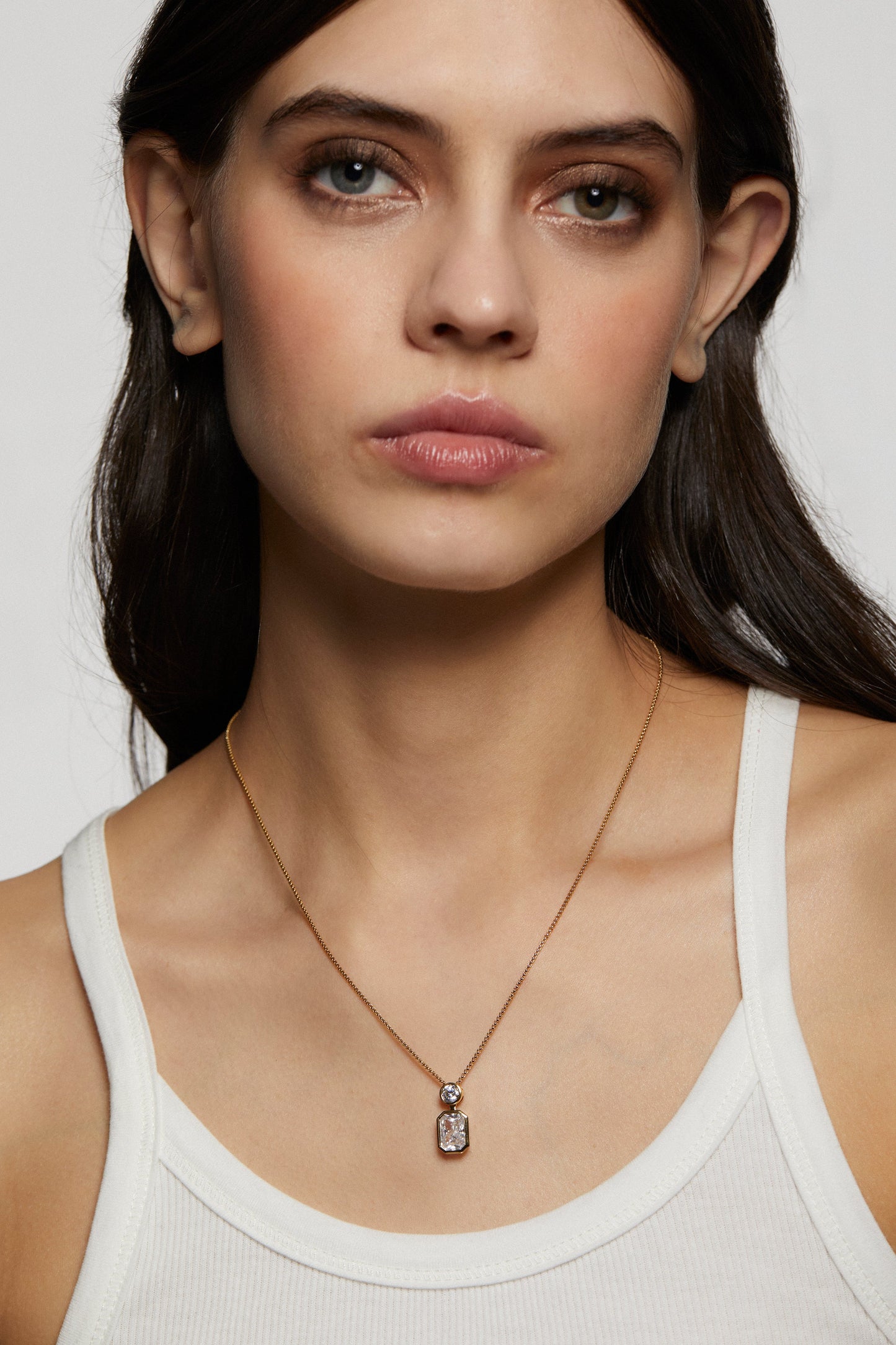 Woman wearing a delicate necklace with a clear pendant on a plain background