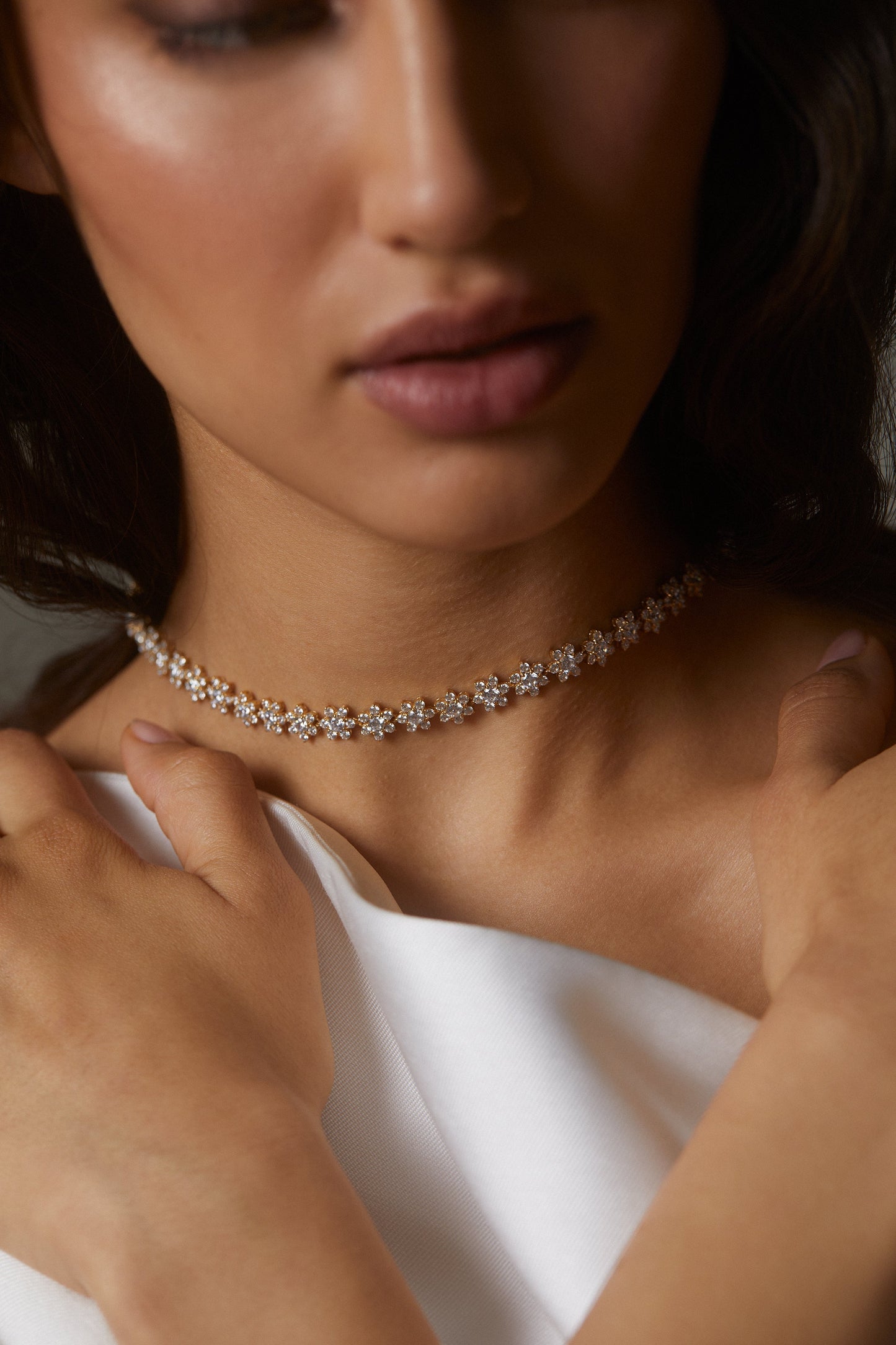 MODEL WEARING DAHLIA FLORAL COLLAR NECKLACE. IT IS A CLOSE UP IMAGE WITH HER FACE BLURRED OUT. SHE IS WEARING A WHITE GOWN. 