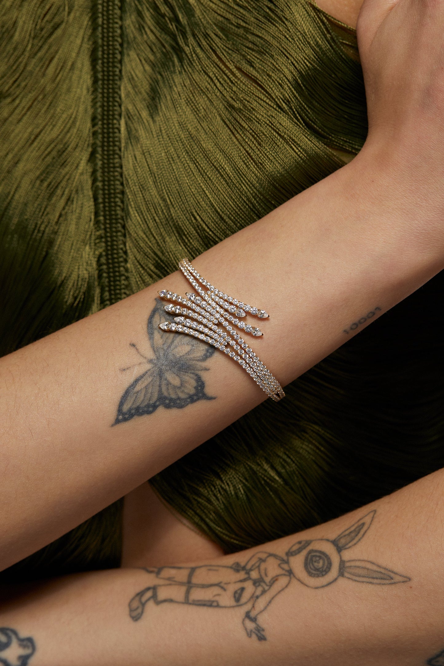 MODEL WEARING DIVA FAN HINGE CUFF. IT IS A CLOSE UP IMAGE OF HER WRIST. SHE IS WEARING A FRINGE GREEN TOP AND HAS A BUTTERFLY TATTOO.