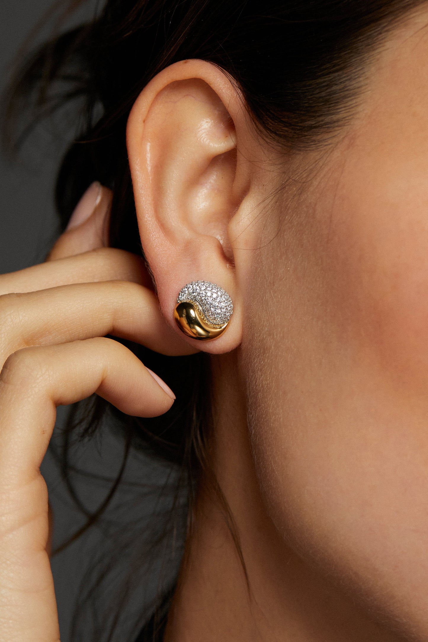 CLOSE UP IMAGE OF MODEL'S EAR WEARING DRIP YIN-YANG STUD EARRINGS. HER HAIR IS A LOOSE BUN AND HER HAND IS REACHING UP TOWARDS THE EARRINGS.