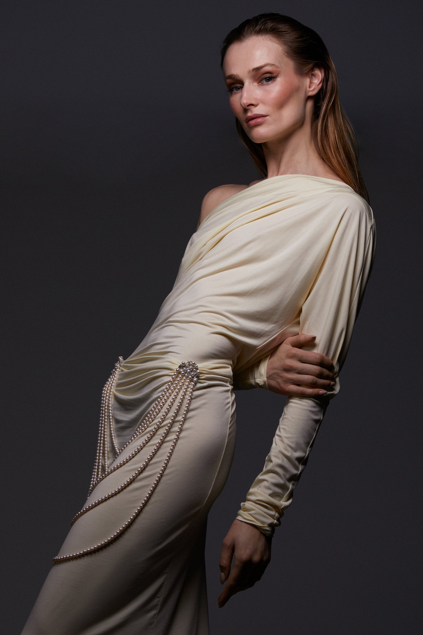 MODEL WEARING INGRID MULTI PEARL STRAND DOUBLE BROOCH ON HER WAIST. HER HAIR IS SLICKED BACK AND SHE IS WEARING A SHEER CREAM OFF THE SHOULDER LONG SLEEVE DRESS. 