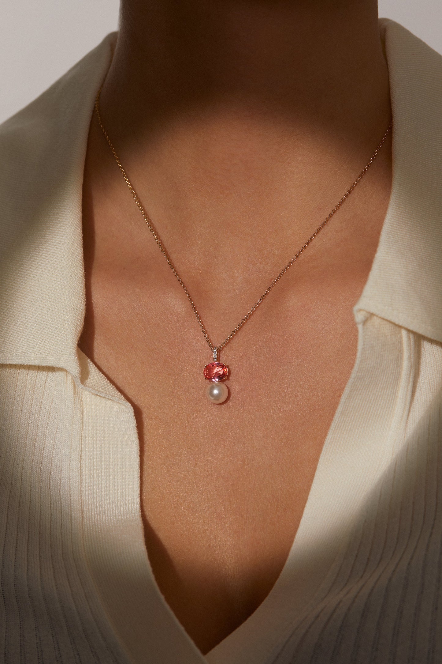 MODEL WEARING NATURAL BEAUTY PINK PEARL PENDANT. IT IS A CLOSE UP IMAGE OF HER NECKLINE. SHE IS WEARING A CREAM V-NECK COLLAR SWEATER TOP.