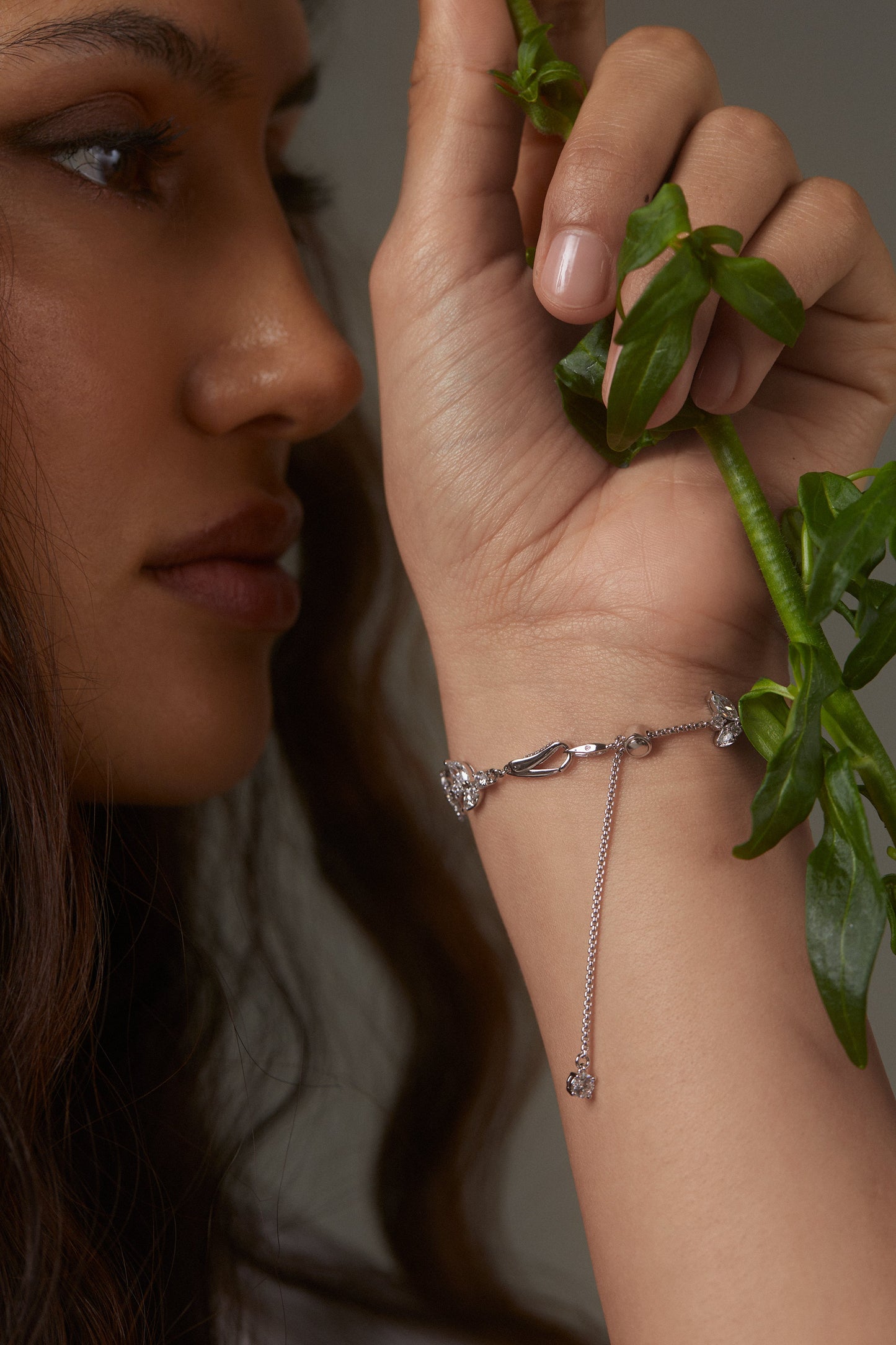 MODEL WEARING RAVISH VINE ADJUSTABLE BRACELET. IT IS A CLOSE UP IMAGE OF HER PROFILE WITH THE BACK OF HER WRIST SHOWING A DETAIL SHOT OF THE CLASP AND ADJUSTABLE BOLO CLOSURE OF THE BRACELET.