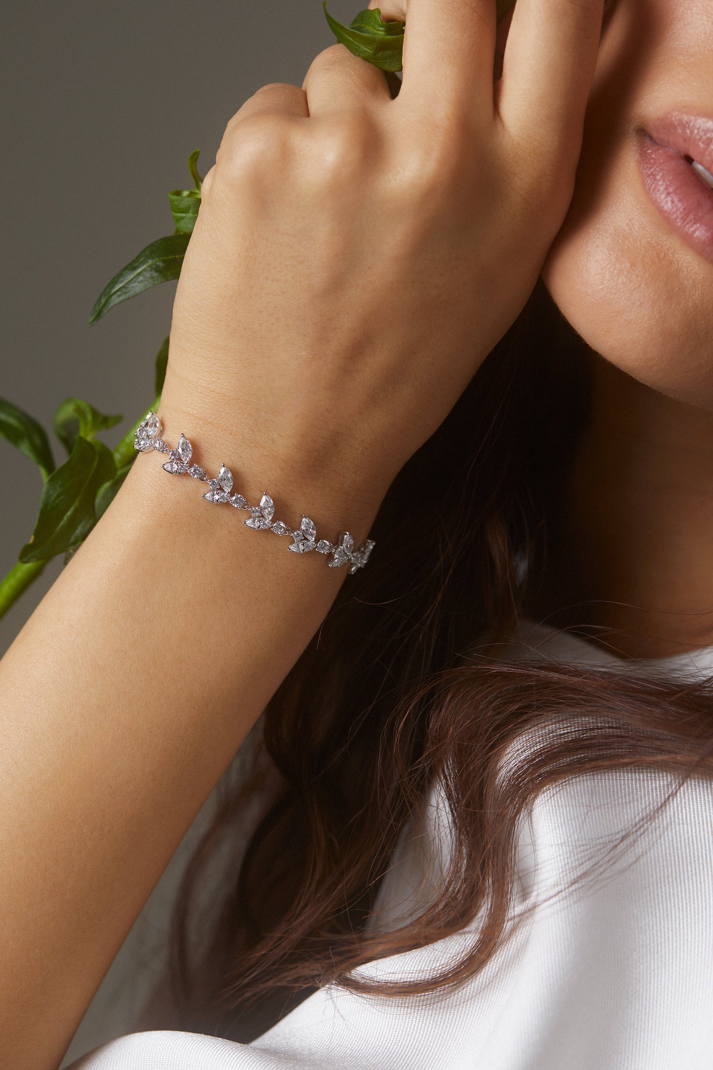 MODEL WEARING RAVISH VINE ADJUSTABLE BRACELET. IT IS A CLOSE UP IMAGE OF HER HAND AND WRIST HOLDING A FLOWER NEAR HER FACE.