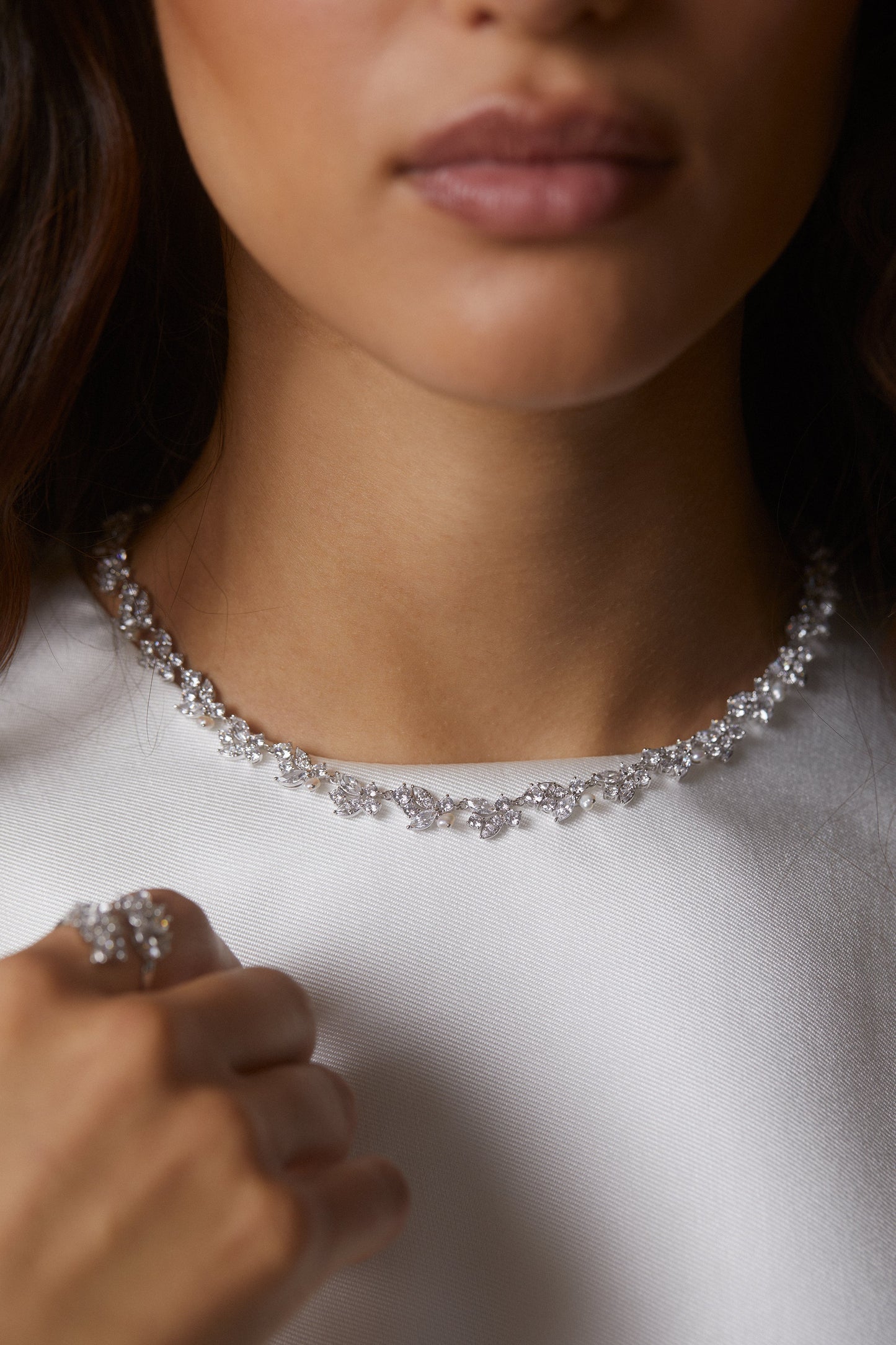 MODEL WEARING RAVISH LAUREL COLLAR NECKLACE. IT IS A CLOSE UP IMAGE CROPPED FROM HER LIPS DOWN SHOWING THE DETAIL OF THE ITEM. SHE IS WEARING A WHITE HIGH NECKLINE TOP.