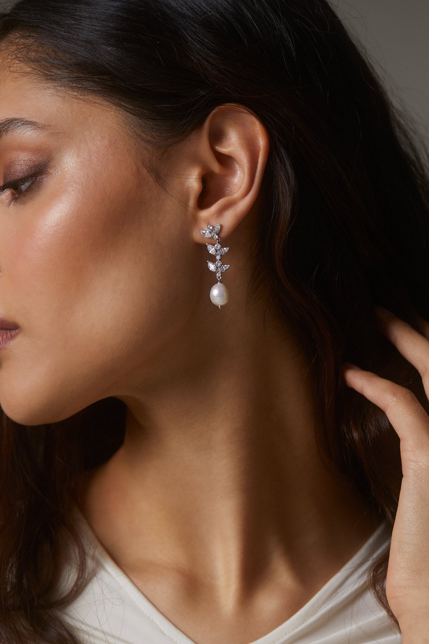 MODEL WEARING RAVISH LINEAR DROP EARRINGS. IT IS A SIDE PROFILE CLOSE UP IMAGE WITH HER DARK BROWN HAIR TUCKED BEHIND HER EARS. 