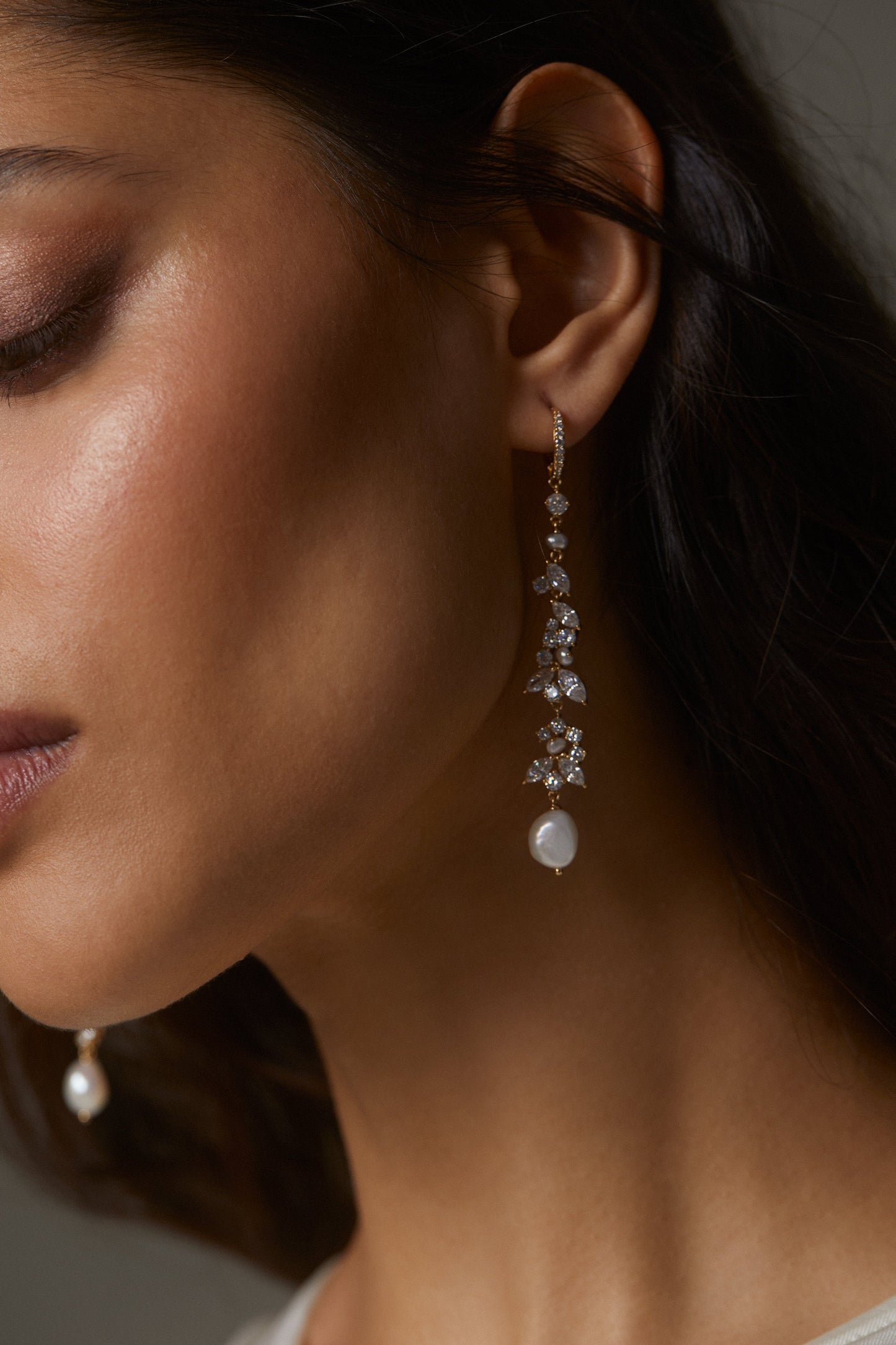 RAVISH LINEAR PEARL LEVERBACK EARRINGS ON MODEL. IT IS A CLOSE UP IMAGE OF HER SIDE PROFILE WITH THE EARRINGS CLEARLY VISIBLE WITH HER DARK BROWN HAIR TUCKED BEHIND HER EARS.