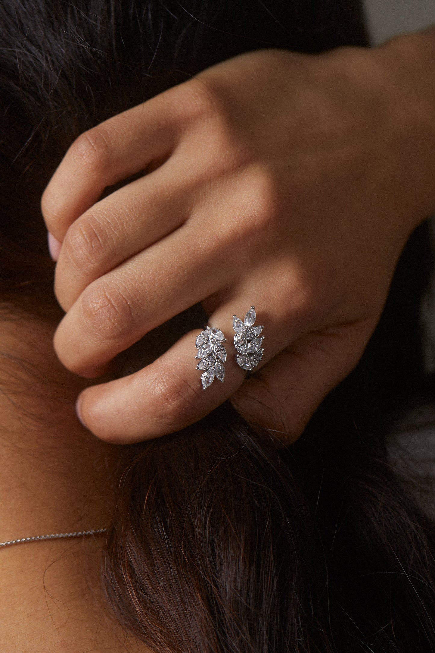 MODEL WEARING THE RAVISH VINE RING. IT IS A CLOSE UP IMAGE OF HER HANDS GRABBING HER HAIR FROM THE BACK OF HER HEAD.