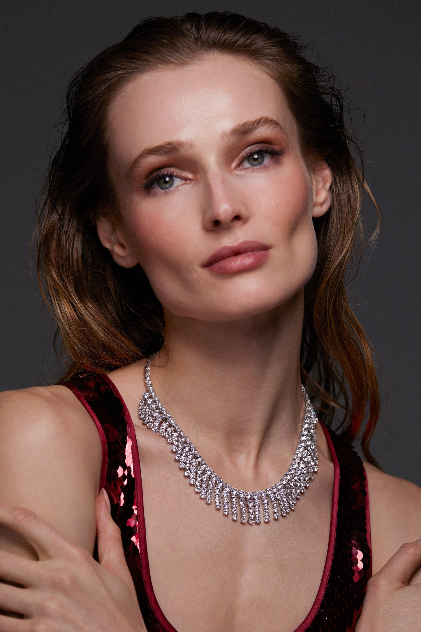 MODEL WEARING STARLET FRINGE NECKLACE. HER ARMS ARE CROSSED AND HER HAIR IS BEHIND HER SHOULDERS WHILE SHE GAZES UP SOFTLY. SHE IS WEARING A RED SEQUIN DRESS.