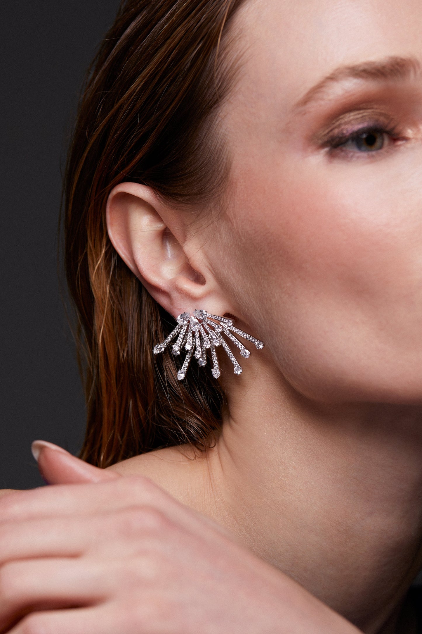 MODEL WEARING STARLET JACKET EARRINGS. ITS A CLOSE UP IMAGE PORTRAIT OF HER FACE WITH HER HAIR TUCKED BEHIND HER EARS. HER HAND IS DRAPPED OVER HER SHOULDER. 