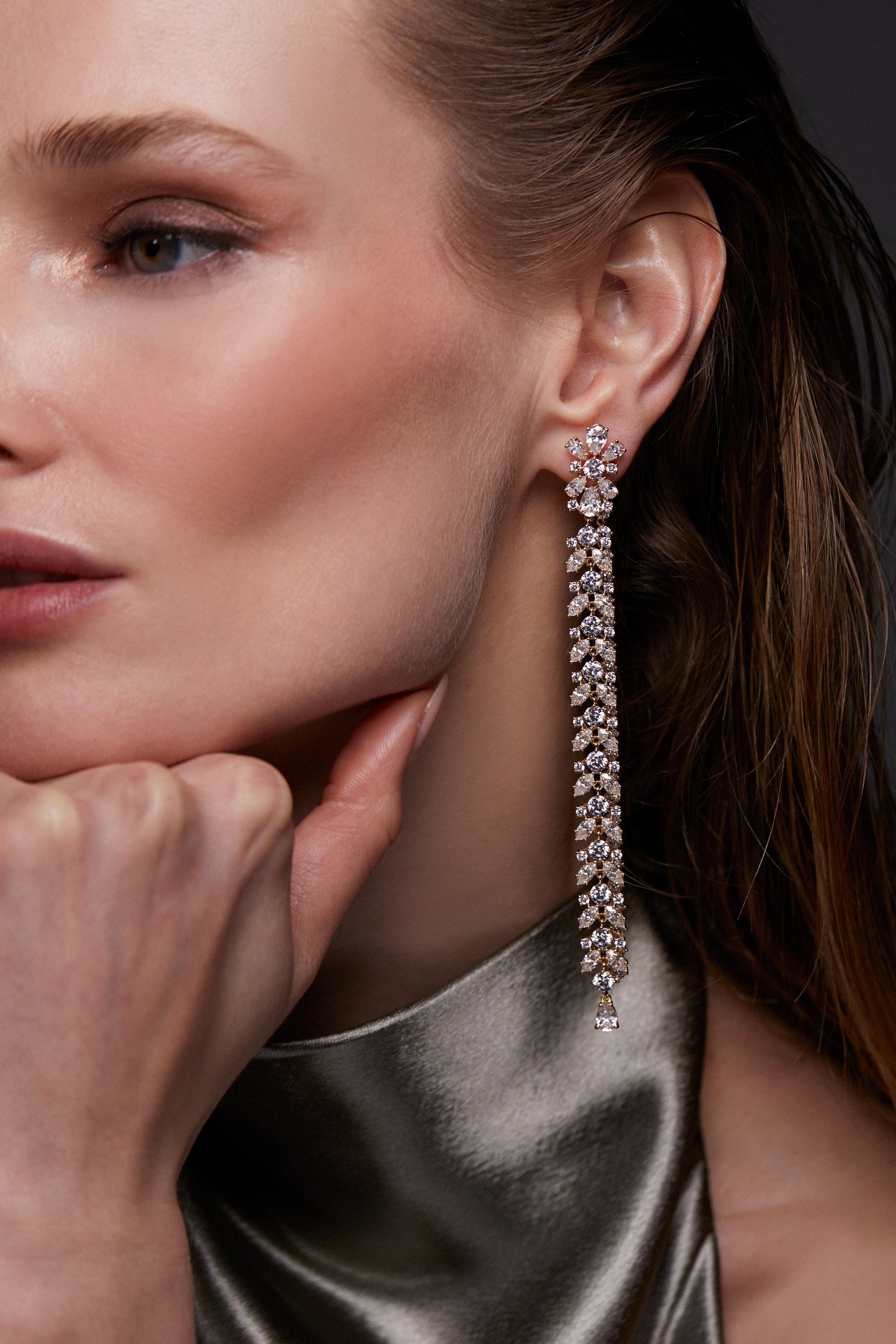 MODEL WEARING STARLET EXTRA LONG LINEAR EARRINGS. IT IS A CLOSE UP PORTRAIT WITH HER HAND ON HER CHIN AND HAIR TUCKED BEHIND HER EARS.