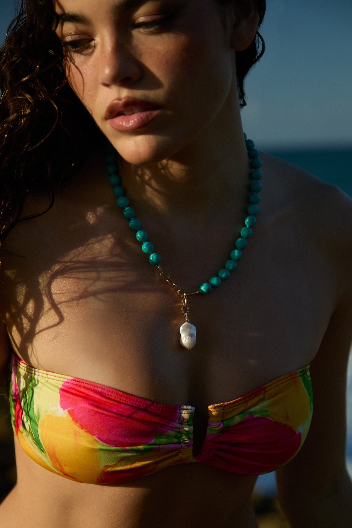 CLOSE UP OF A MODEL’S CHEST WITH HER HAIR TO THE SIDE, WEARING A FLORAL BIKINI AND THE BEADS OF PARADISE FRESHWATER PEARL ADJUSTABLE Y NECKLACE