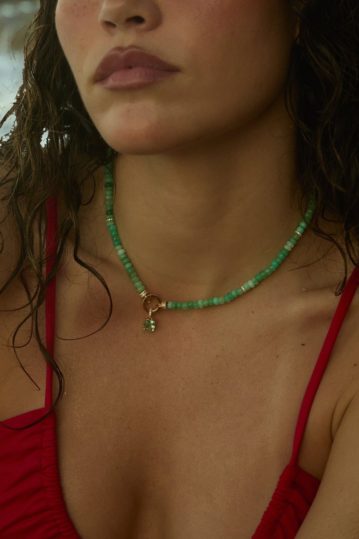 CLOSE UP OF A MODEL’S CHEST AS SHE WEARS A RED BATHING SUIT TOP AND THE BEADS OF PARADISE GREEN CUSHION PENDANT NECKLACE