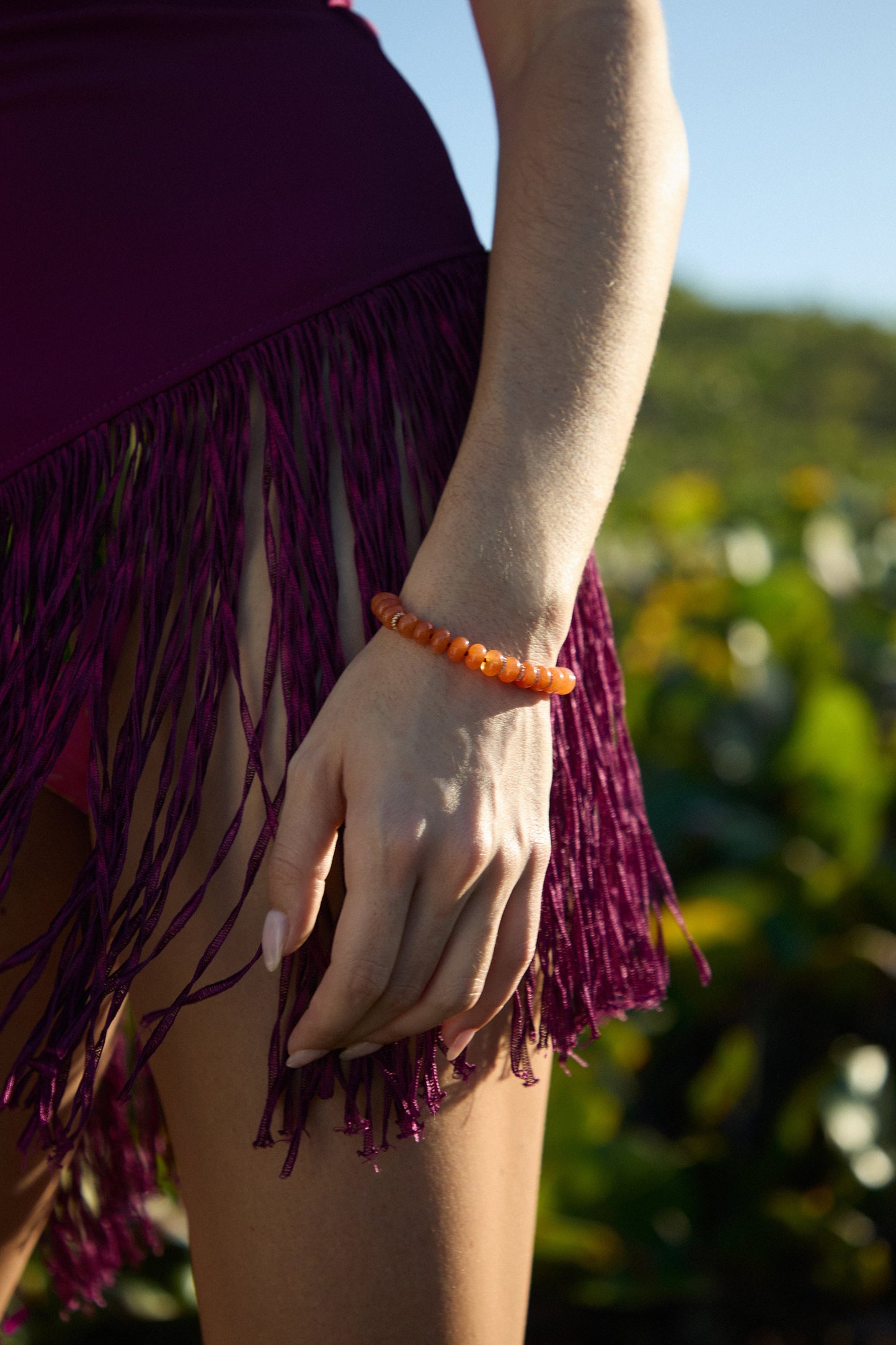 CLOSE UP OF A MODEL’S HAND AT HER SIDE, WEARING A PURPLE COVER UP AND THE BEADS OF PARADISE AMZ RNDL BOLO BRACELET