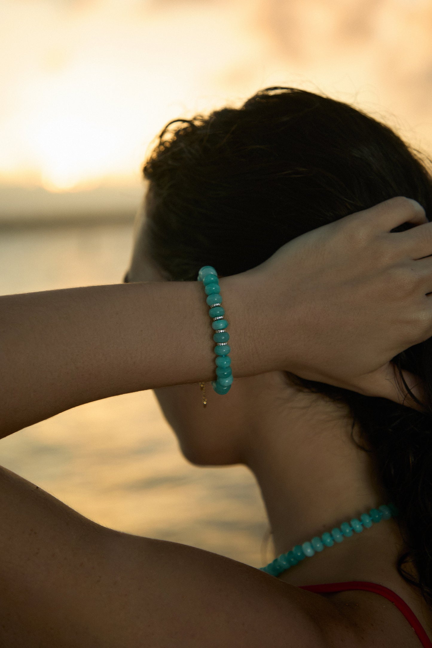 CLOSE UP OF A MODEL’S HAND RUNNING THROUGH HER HAIR, WEARING THE BEADS OF PARADISE AMZ RNDL BOLO BRACELET