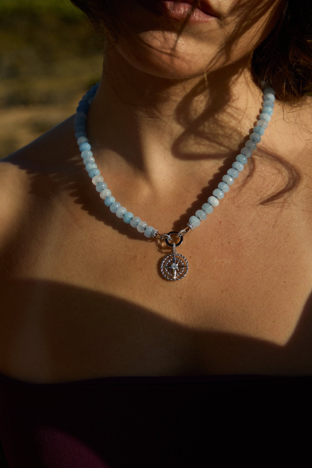 CLOSE UP OF A MODEL’S CHEST WEARING THE BEADS OF PARADISE NAUT PENDANT NECKLACE, AS THE SUN SHINES ON IT