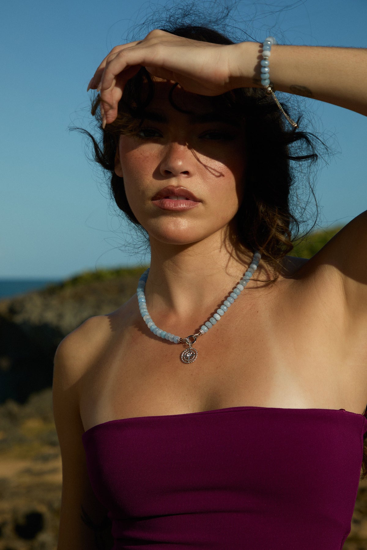 MODEL WEARING A PURPLE TOP WITH HER HAND UP TO HER FACE BLOCKING THE SUN, WEARING THE BEADS OF PARADISE NAUT PENDANT NECKLACE