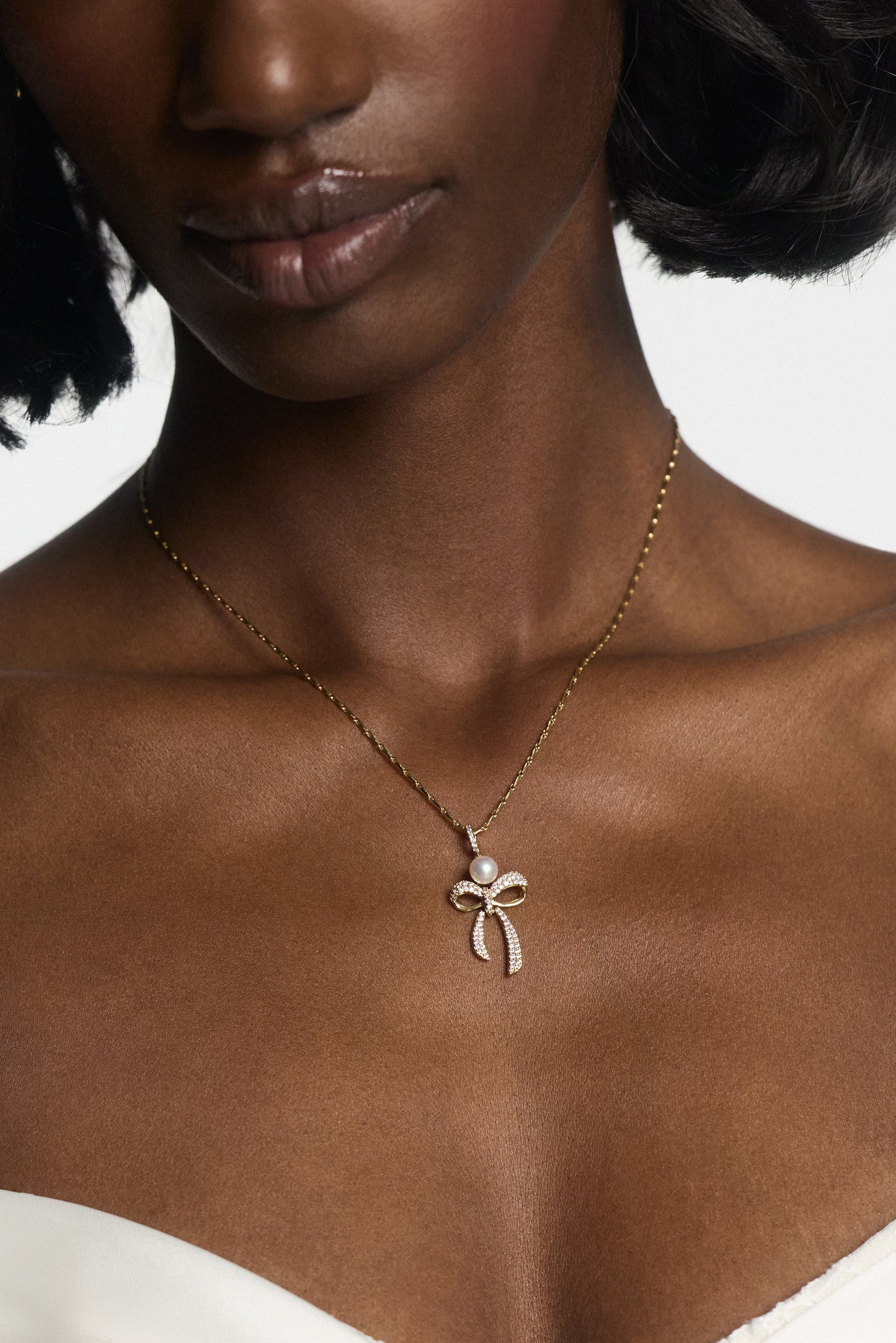 CLOSE UP OF A MODEL’S CHEST AND NECK, AS SHE WEARS NADRI’S EROS BOW AND PEARL PENDANT NECKLACE