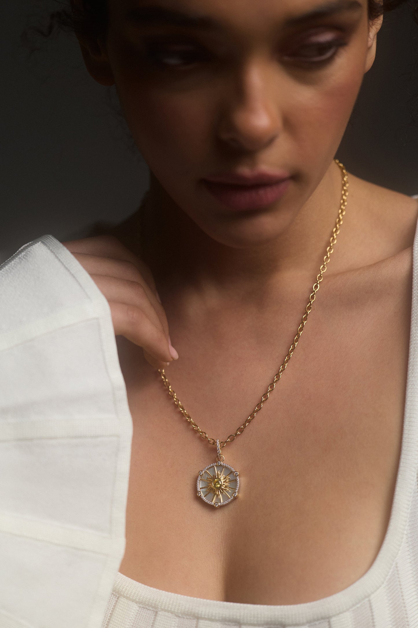CLOSE UP OF A MODEL LOOKING DOWN WITH HER HAND LIFTED TO HER CHEST, WEARING A WHITE TOP AND THE GLOBE TROTTER SUN PENDANT NECKLACE