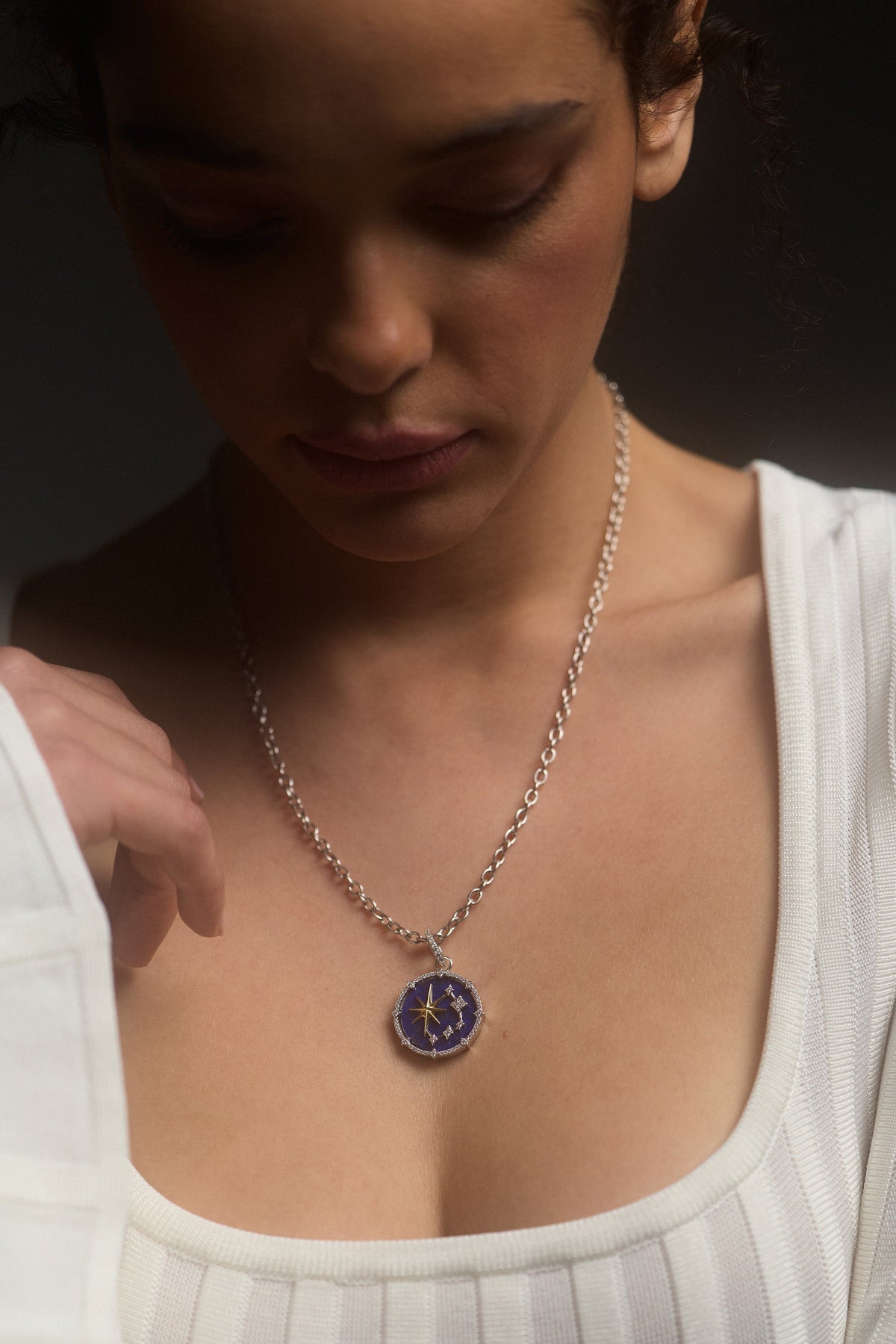 CLOSE UP OF A MODEL LOOKING DOWN, WEARING A WHITE TOP AND THE GLOBE TROTTER STARS PENDANT NECKLACE
