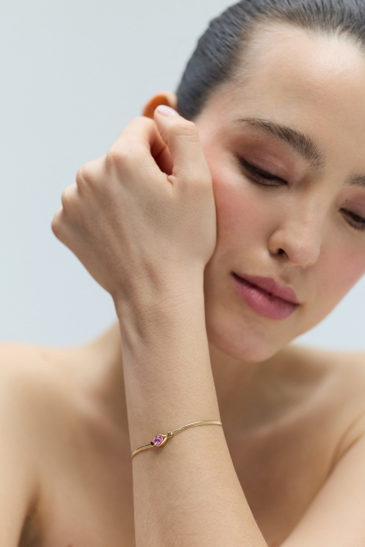 CLOSE UP OF A MODEL LOOKING DOWN WITH HER WRIST LIFTED UP TO HER FACE, WEARING THE DELANCEY PINK PEAR LINE BRACELET
