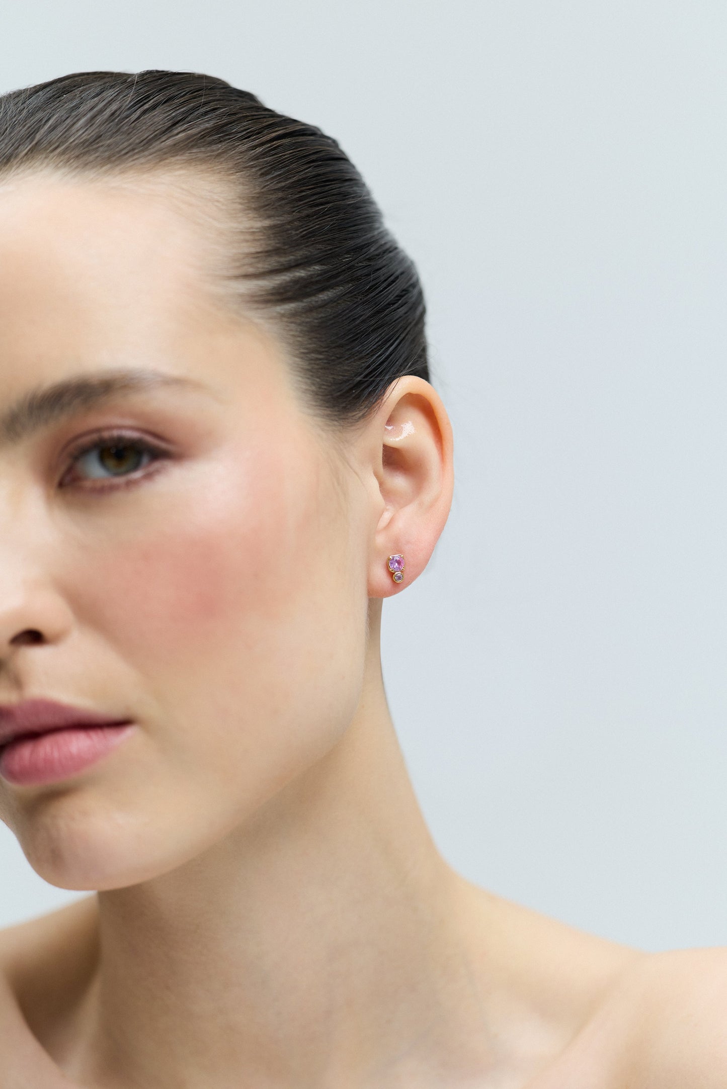 HALF OF A MODEL’S FACE WITH HER EAR IN FOCUS, WEARING THE DOUBLE STONE STUD FROM THE DELANCEY PINK STUD SET OF EARRINGS