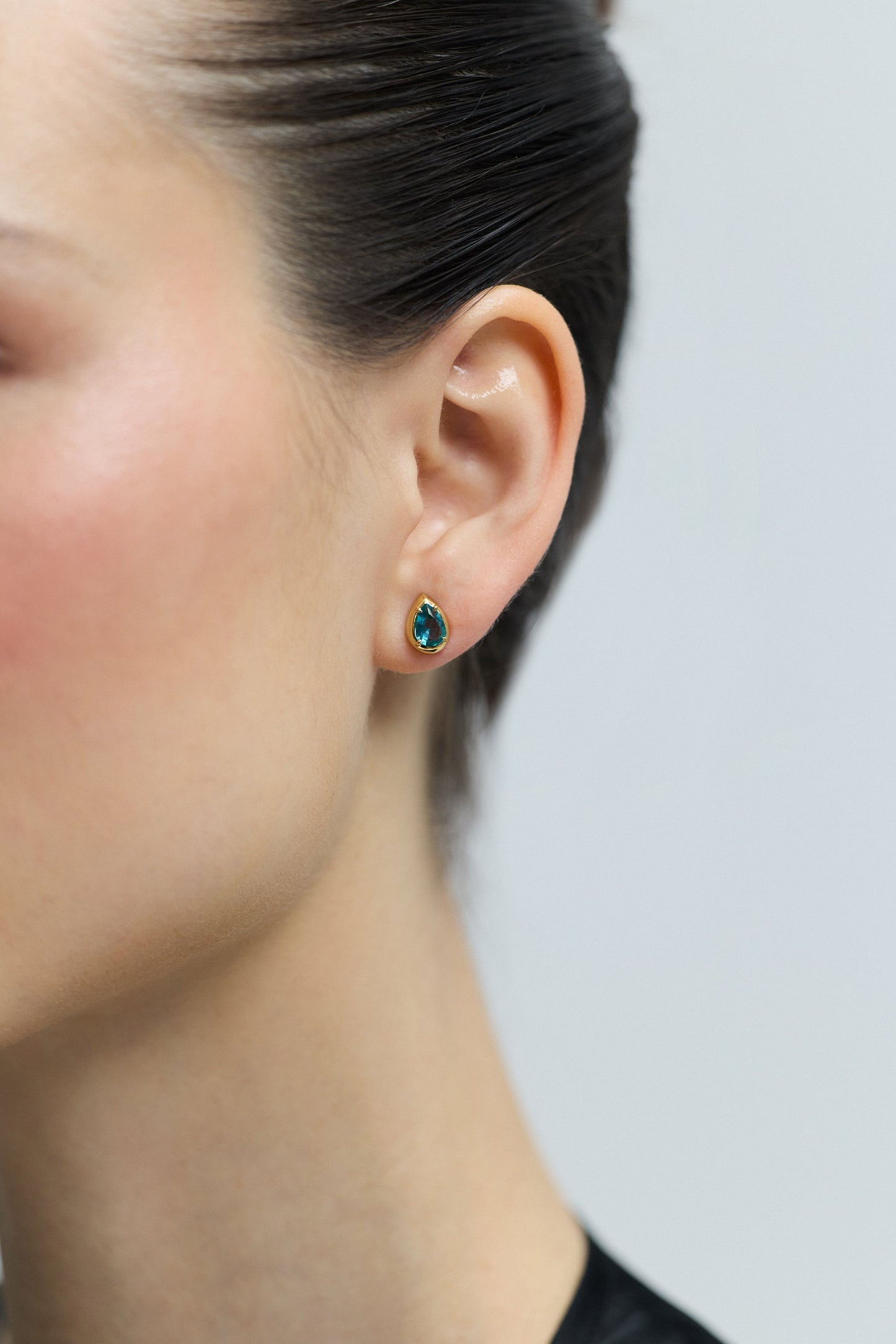 CLOSE UP OF A MODEL’S EAR WEARING THE PEAR STUD FROM THE DELANCEY AQUA STUD SET OF EARRINGS